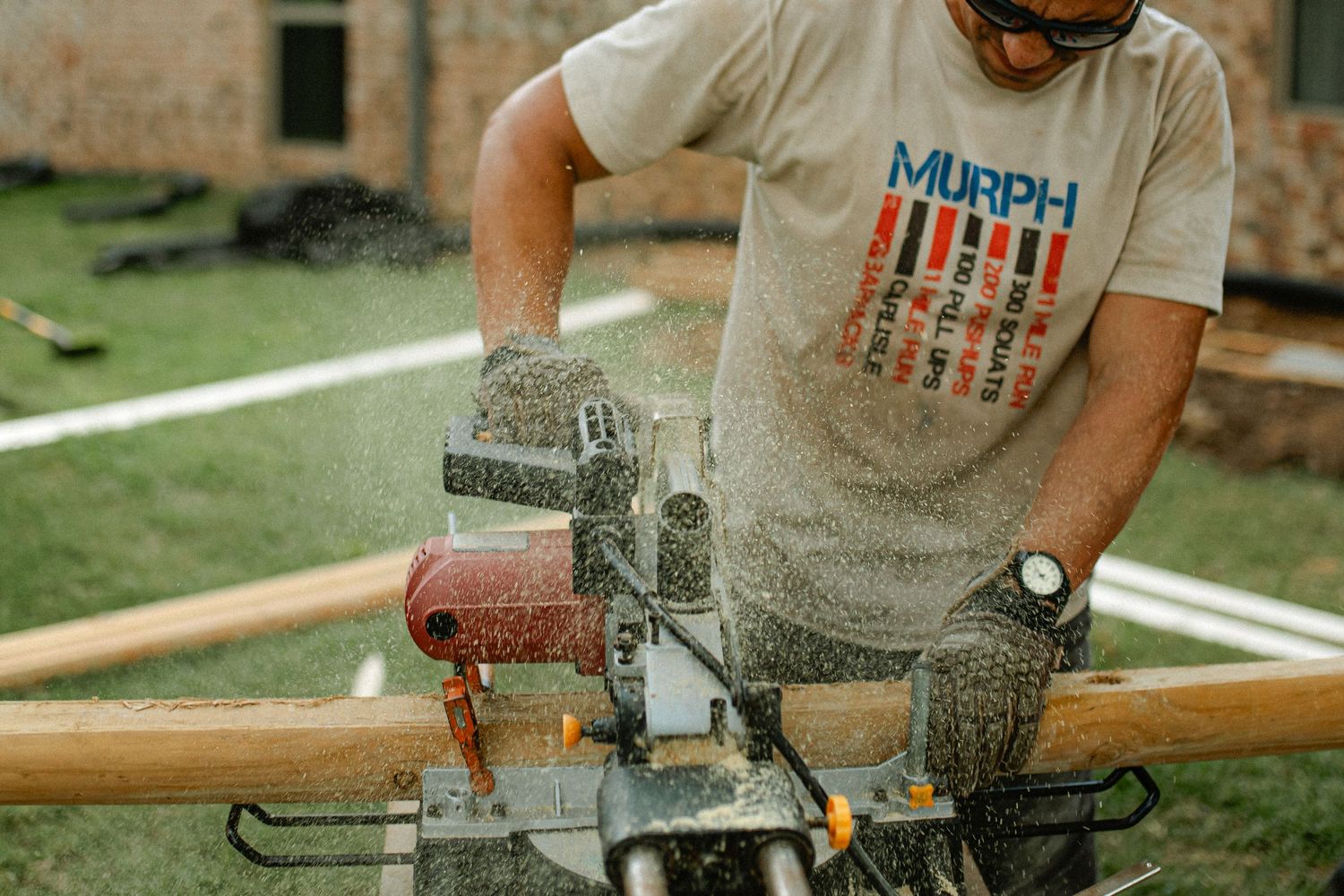 Construction worker using power tools to cut through wood and create dust clouds at outdoor worksite. Documentary Photographer Liz Perez