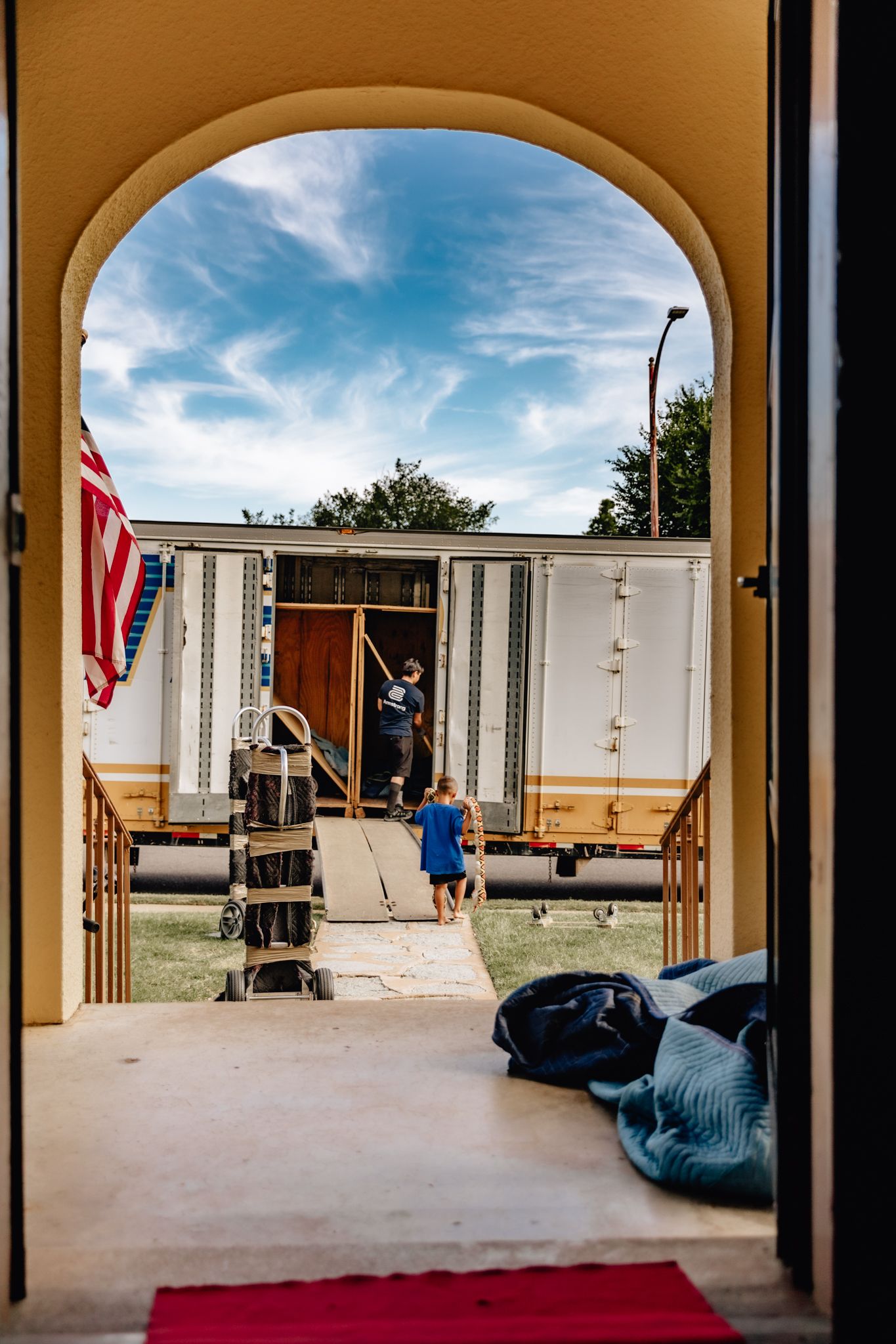View through an arched doorway showing a mobile home entrance with an American flag and blue sky overhead.