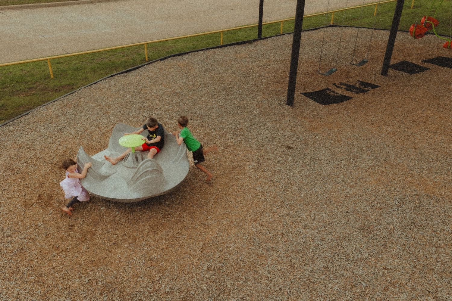 Aerial view of children playing on spinning playground equipment at park.