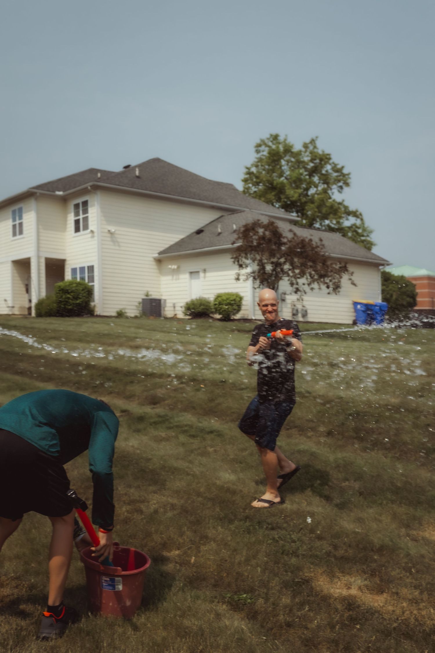 Summer water fight scene with people spraying each other in a residential backyard.