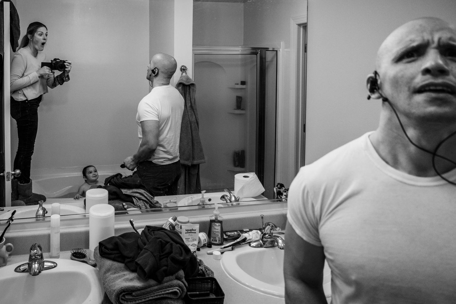 Black and white photo showing a dressing room with multiple mirrors and personal items scattered on the counter.
