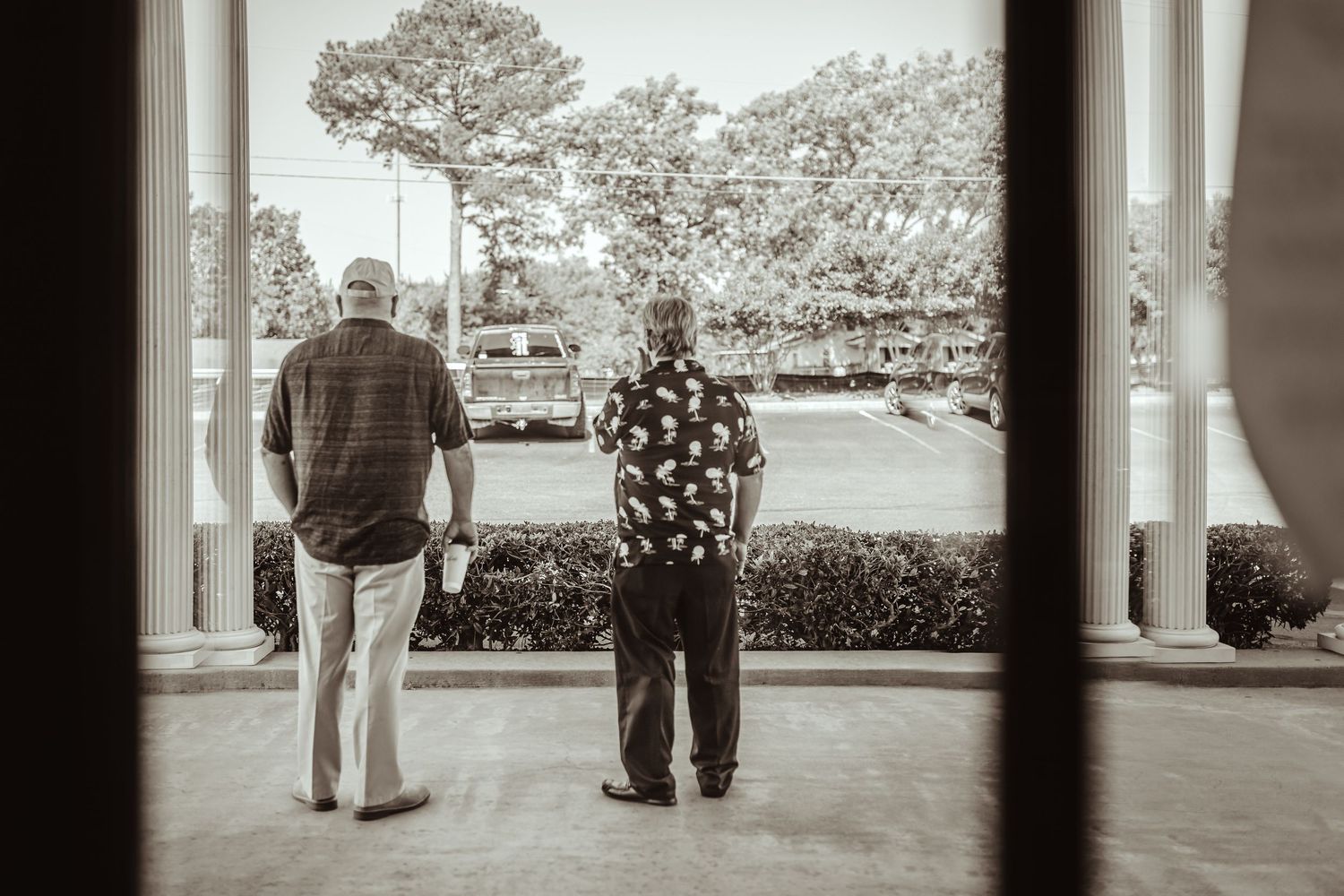 Two people stand in silhouette on a covered porch overlooking a landscaped garden.
