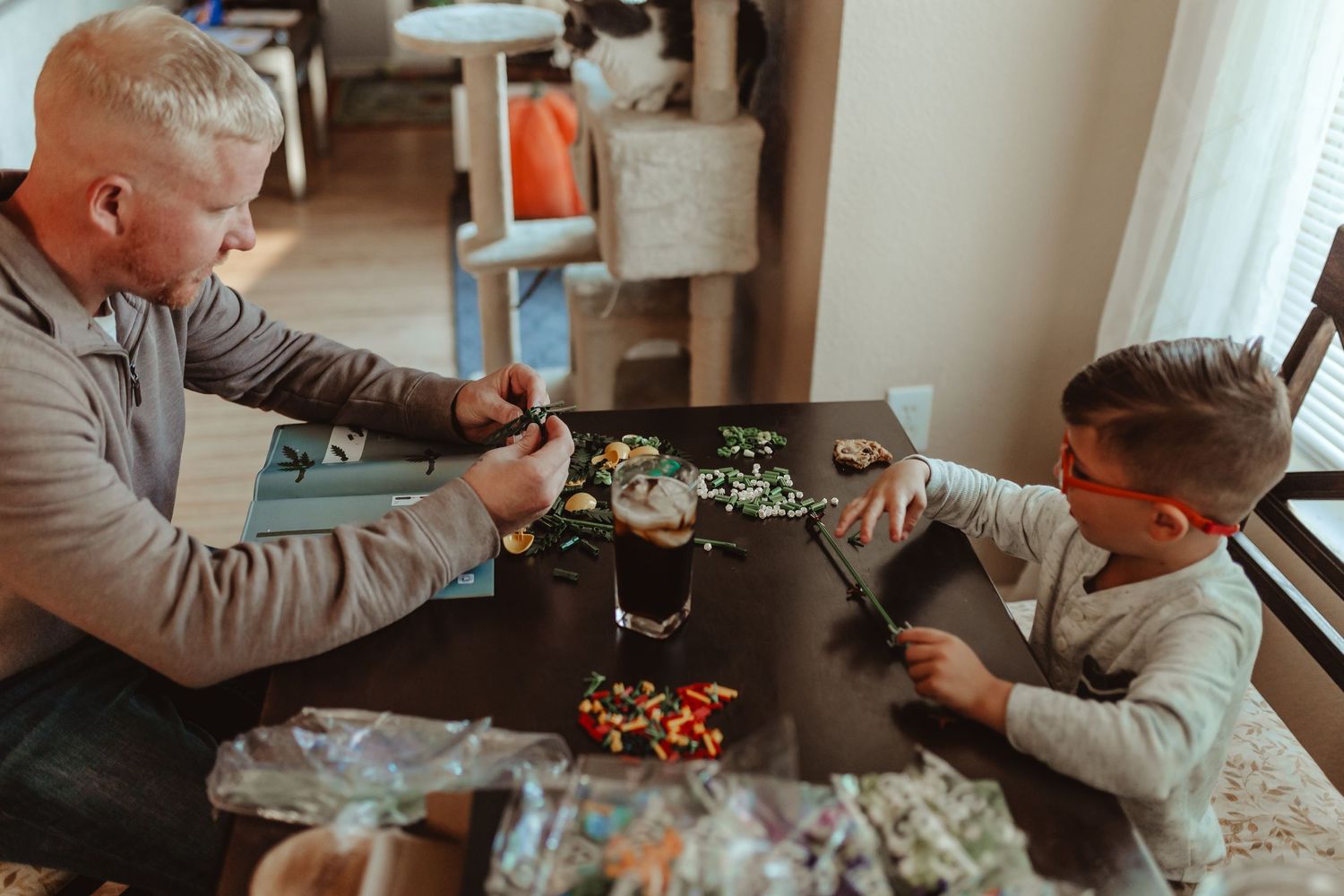 Two people playing with small toys at a wooden table.