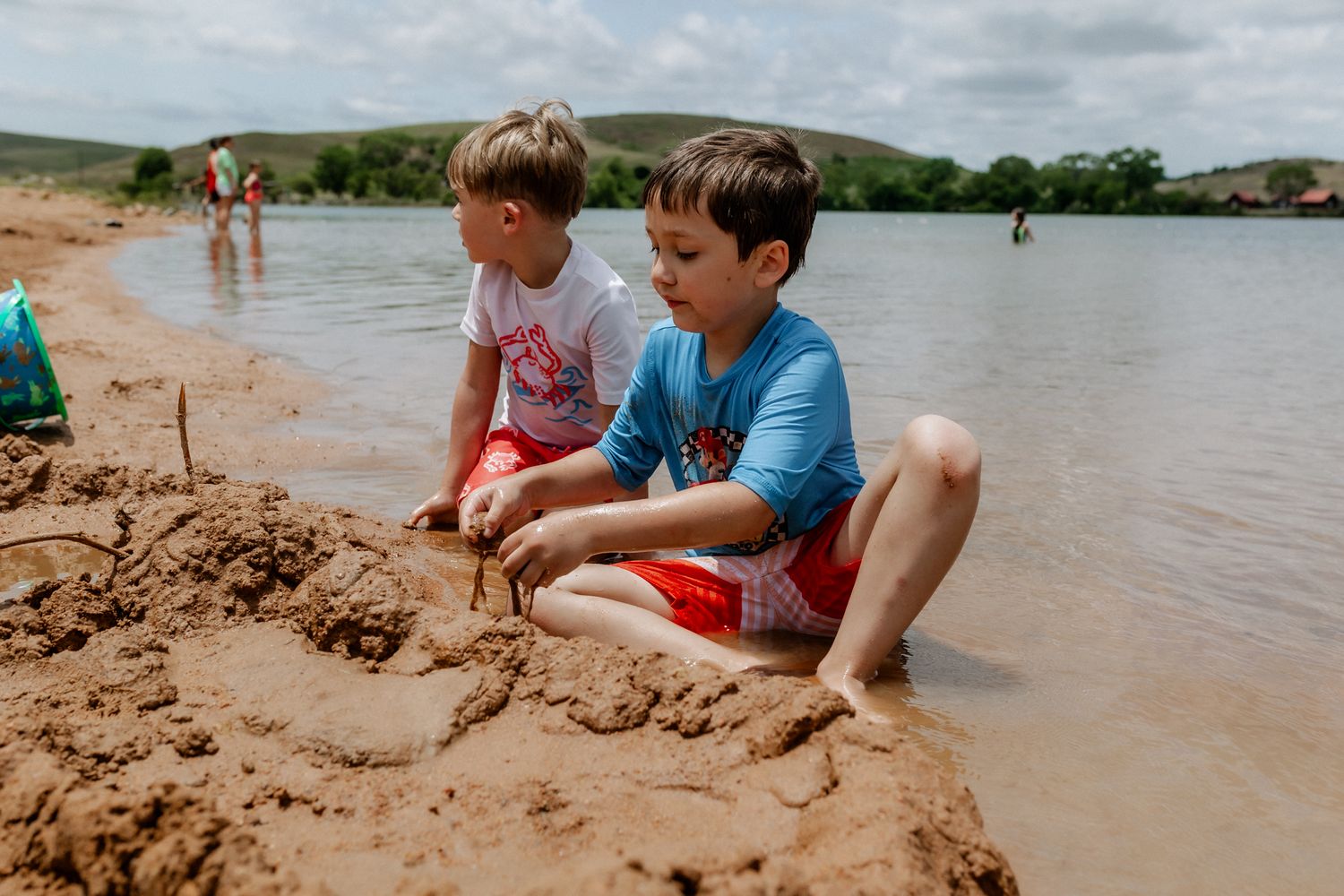 Children playing in wet sand at the edge of a muddy lake or beach.