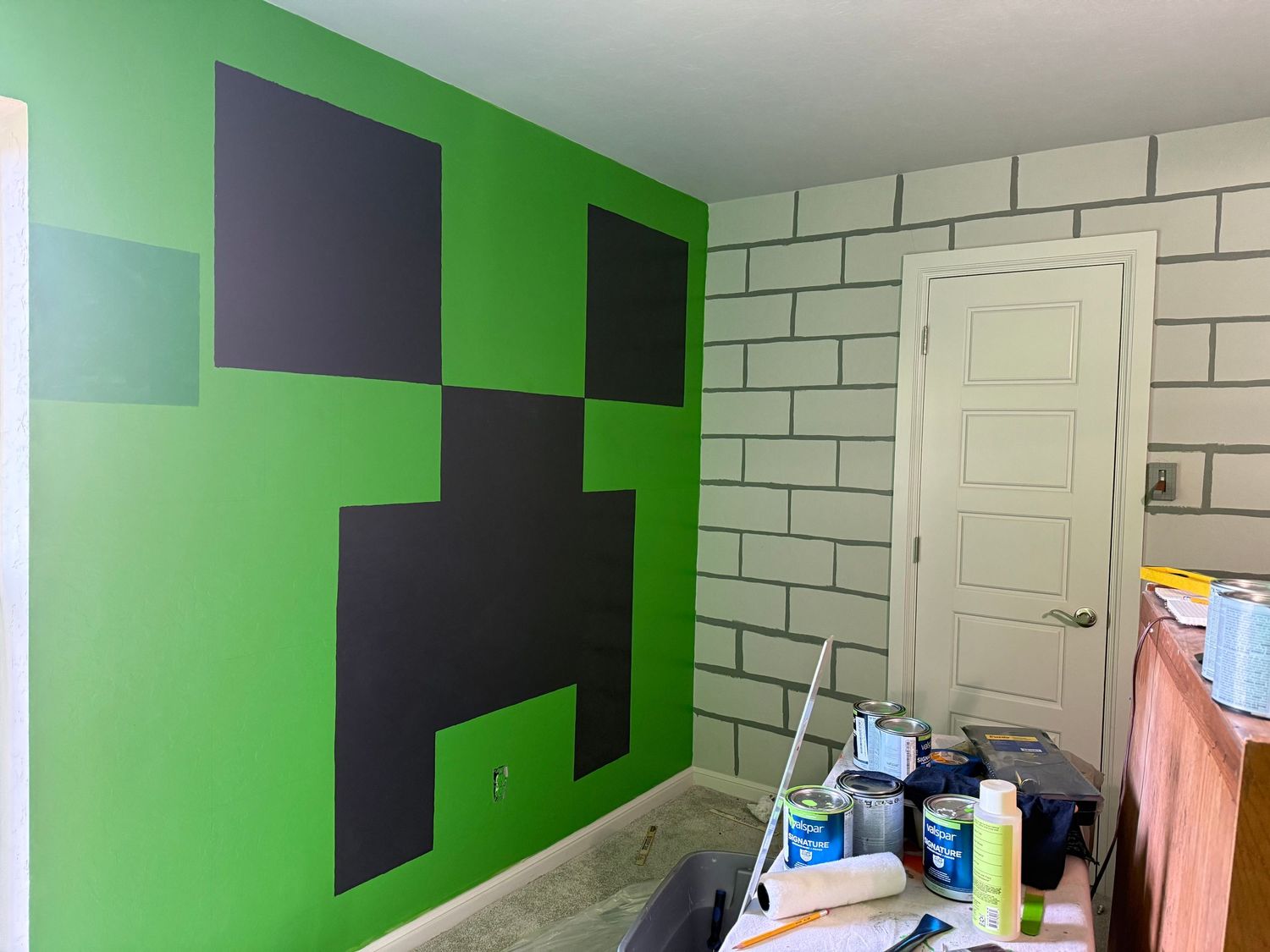 progress photos show a bedroom wall being painted with alternating green and black squares in a Minecraft-inspired design.
In-Home Photogra