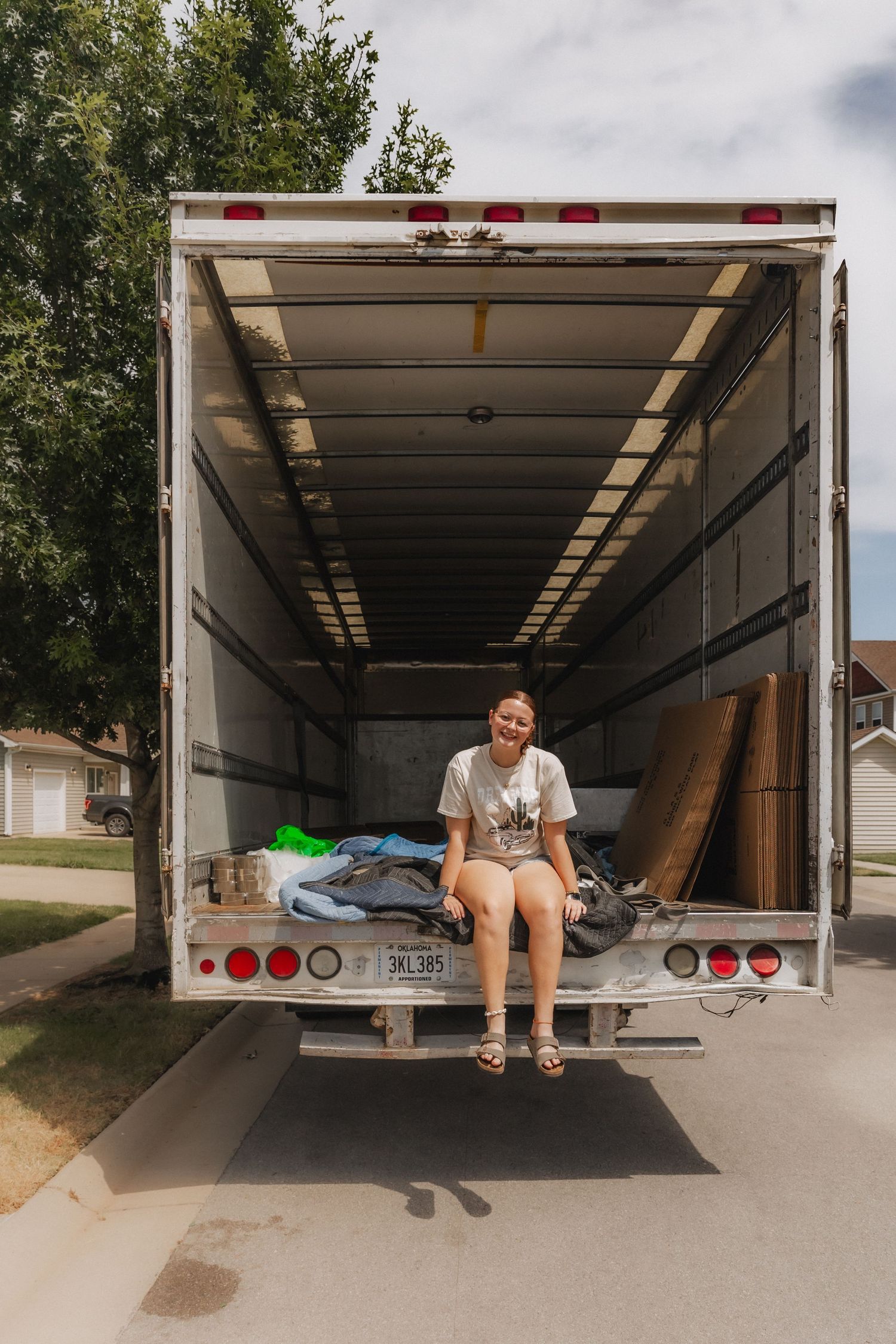 Woman sitting on the edge of an open moving truck parked in a residential driveway.