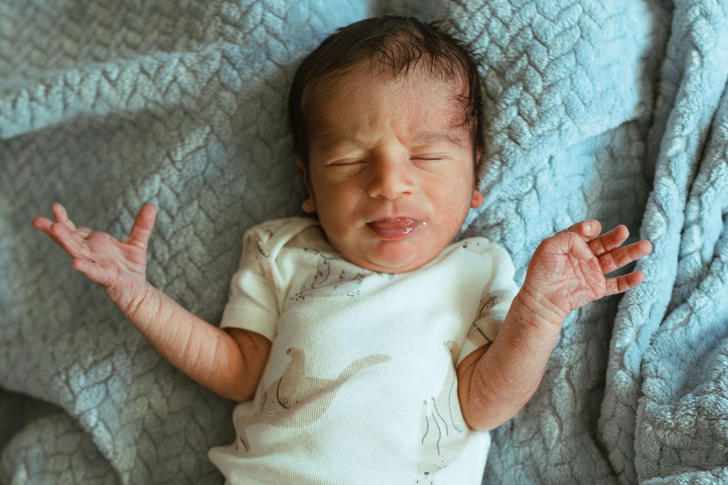 Baby resting on a blue knitted blanket in soft natural lighting.