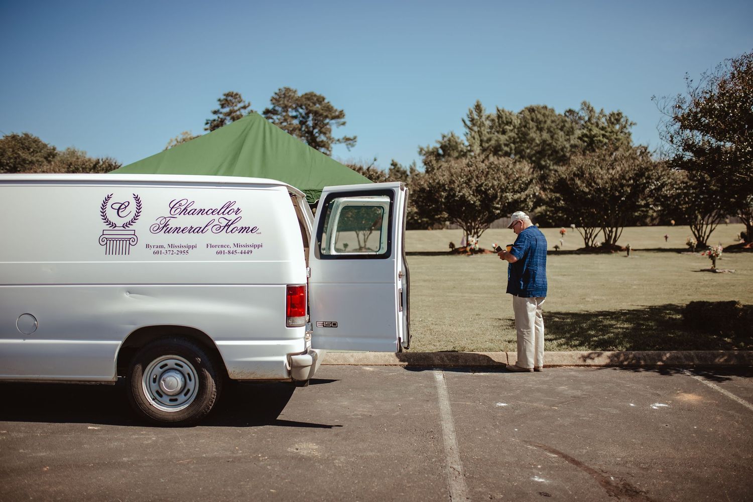 A white funeral home van parked in an outdoor lot with funeral services signage visible.