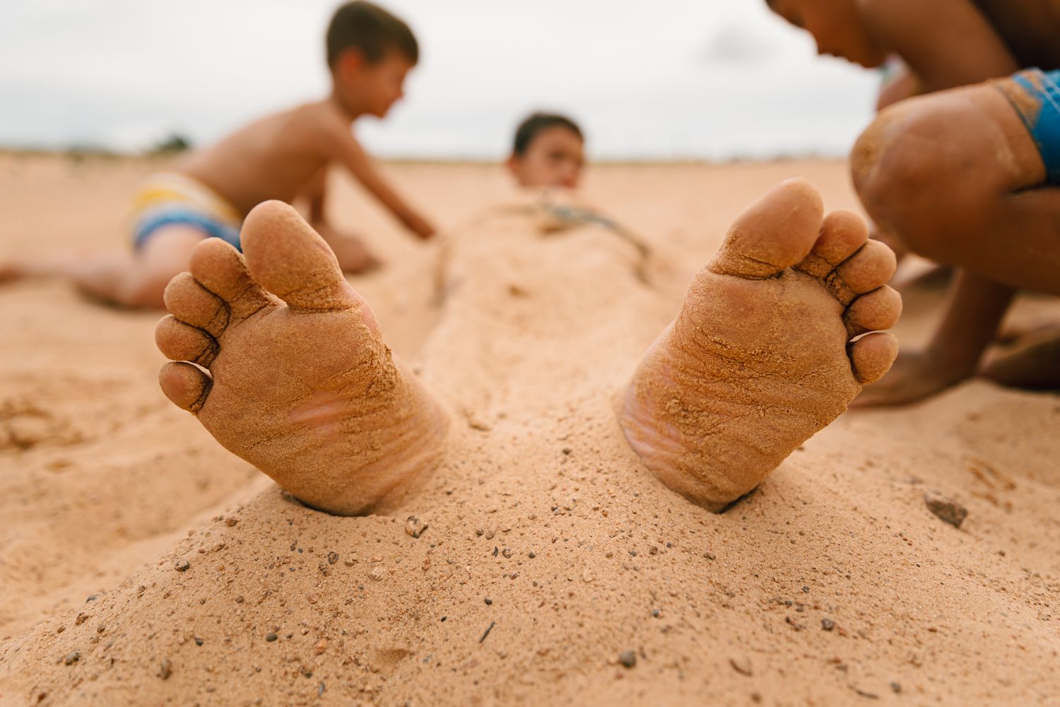 Close-up of bare feet on sandy beach surface in warm sunlight.