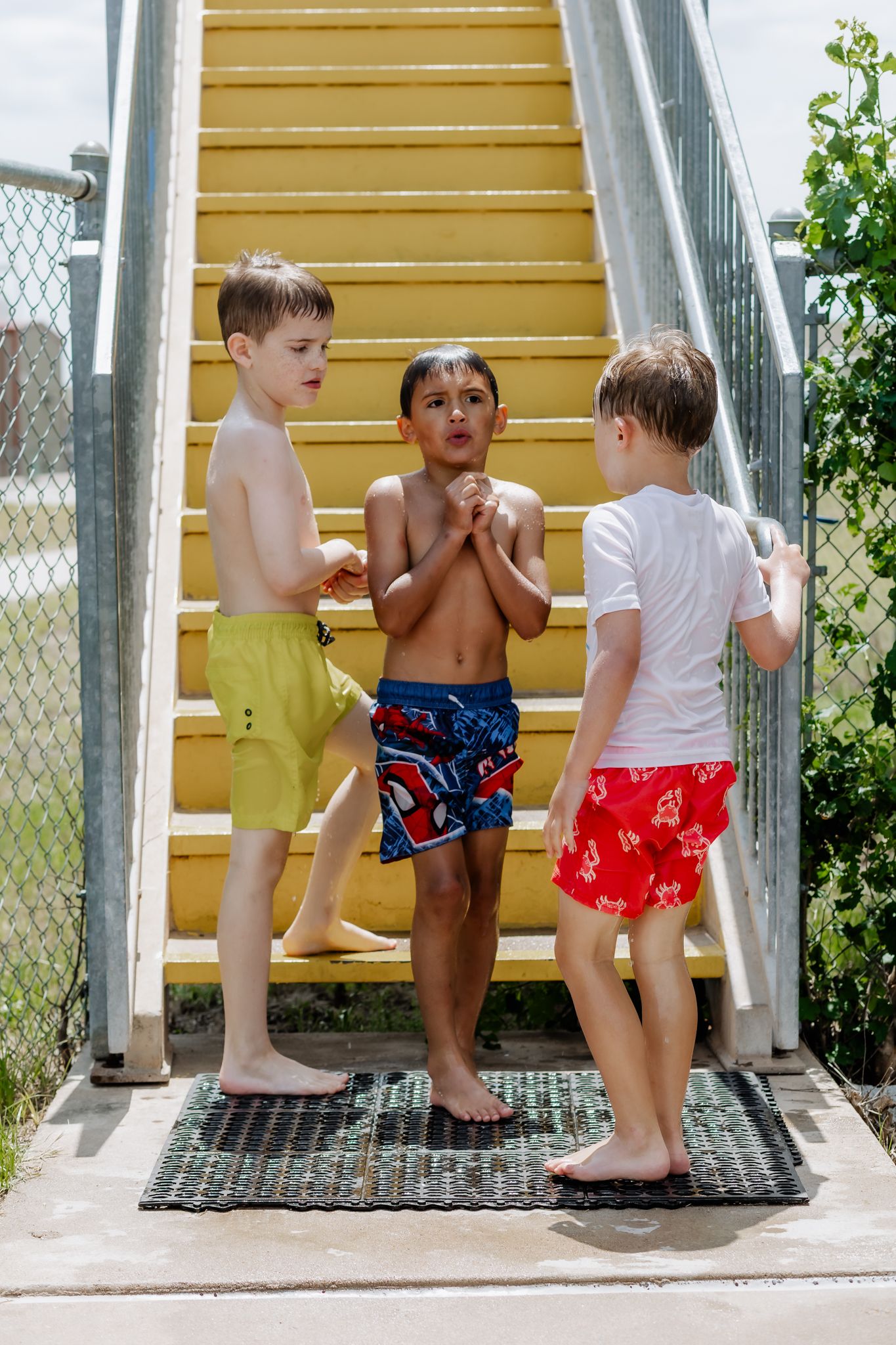 Children in swimming attire gathered on metal steps at an outdoor pool.