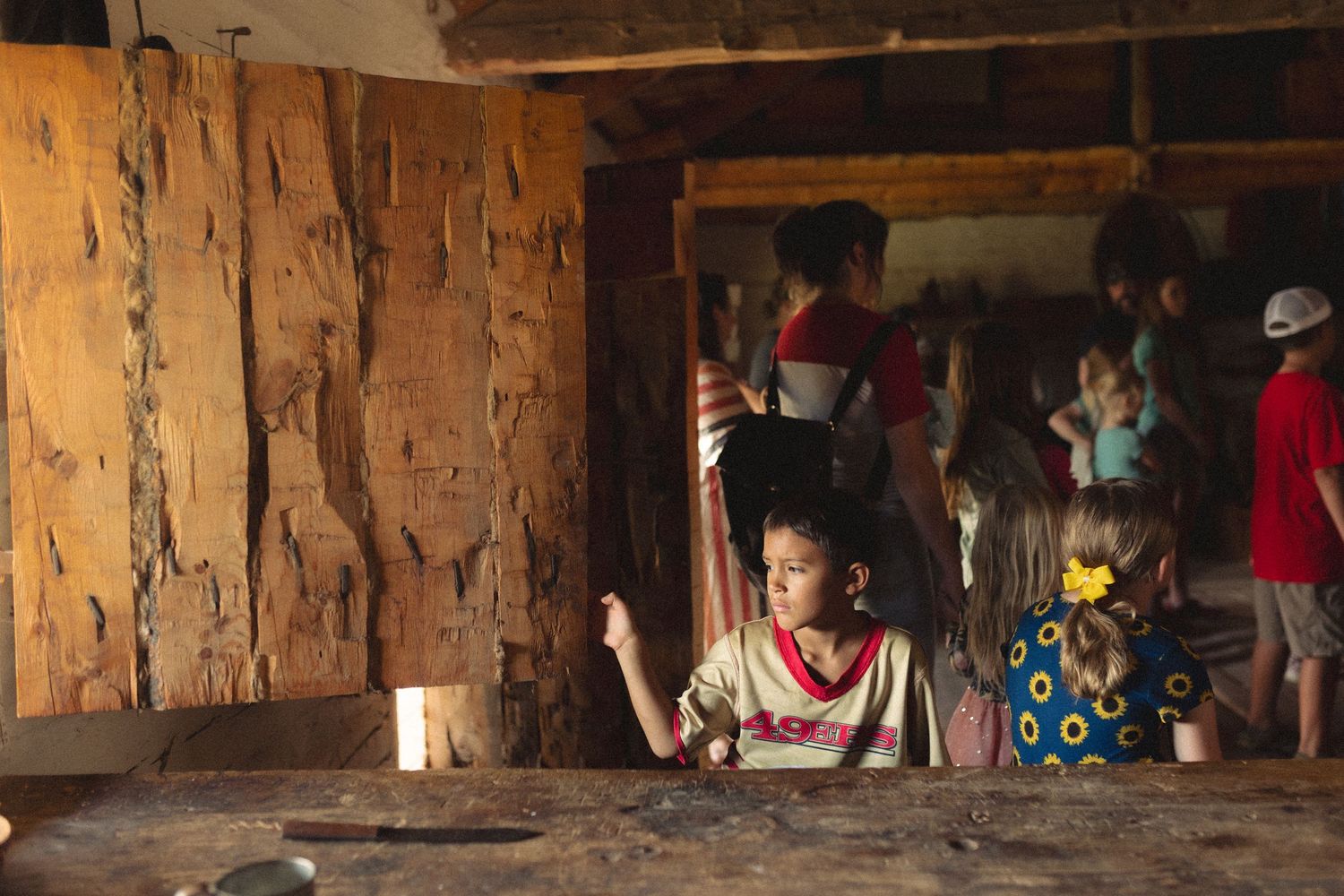 Local community members gather inside a rustic wooden structure with exposed timber walls and dim lighting.
