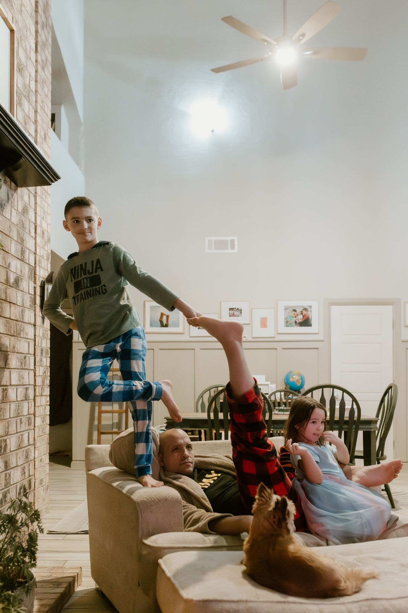 Group relaxing on couch with dog while one person balances on armrest.