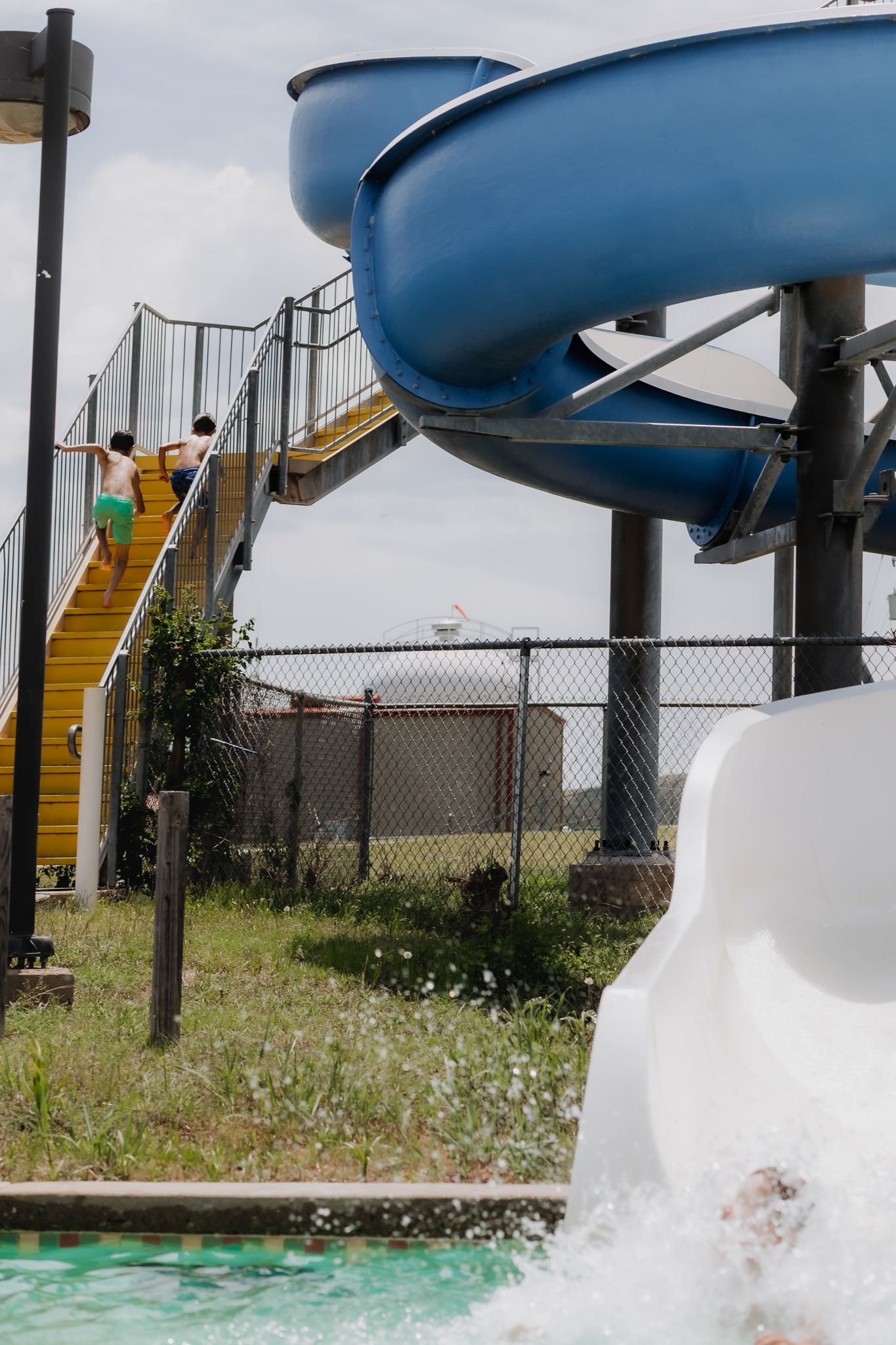 View of curved water slide structure with stairs and blue tubes at outdoor pool.