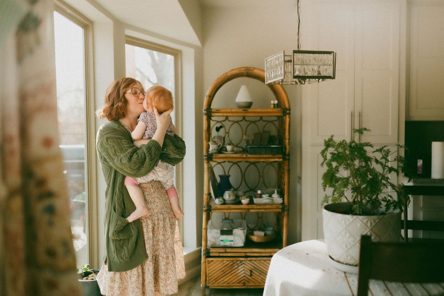 A cozy interior scene with natural light streaming through windows, featuring a decorative shelf unit and potted plants.