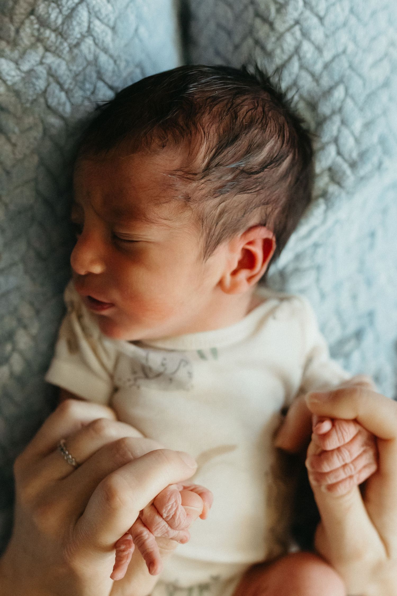 Close-up of a sleeping newborn baby wearing a white onesie against a textured blanket.