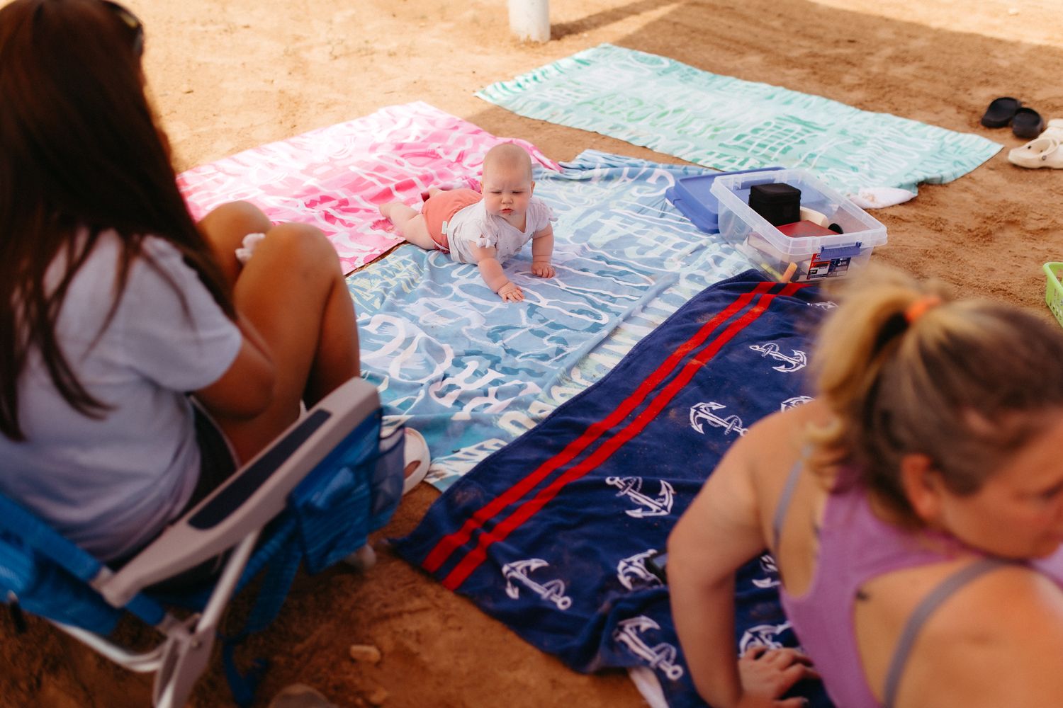 People relaxing on beach blankets with nautical anchor patterns.