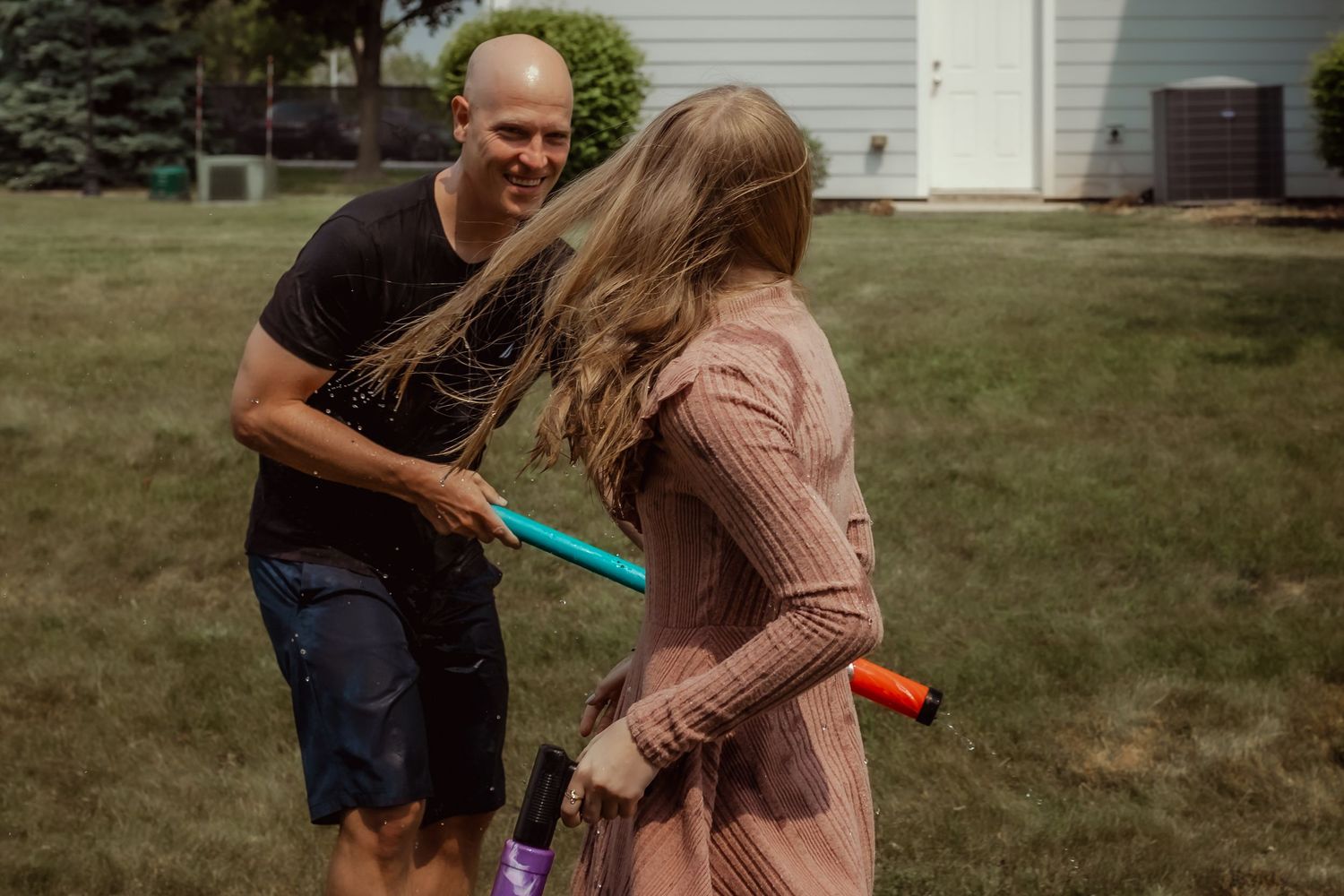 People having a playful water fight with colorful water guns in front of a house.