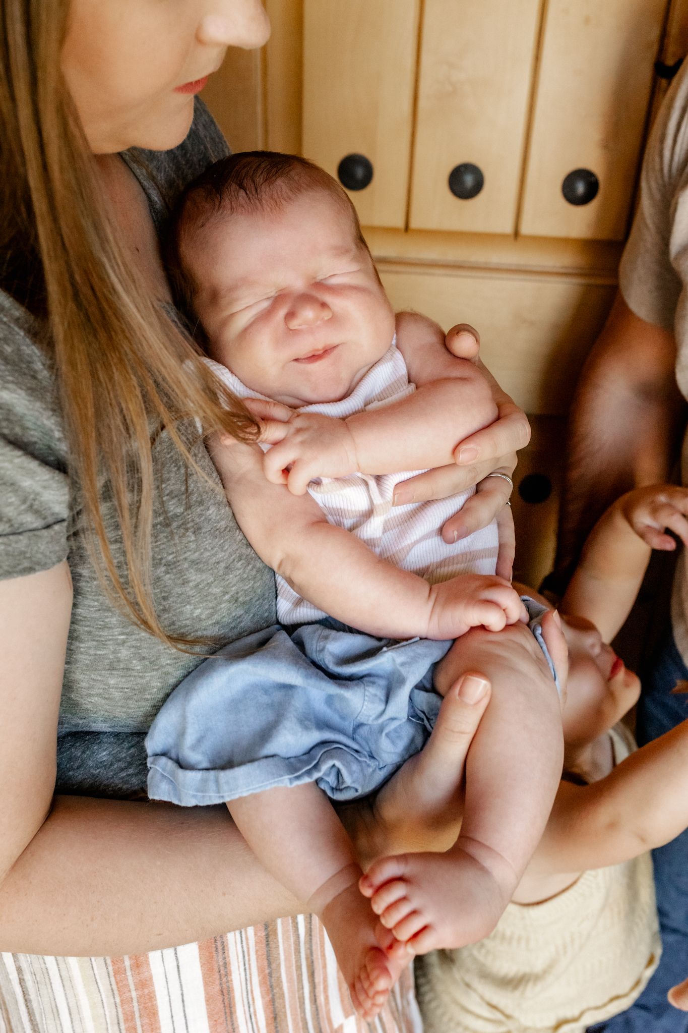 A tiny sleeping newborn baby wearing light blue clothing being cradled gently in someone's arms.