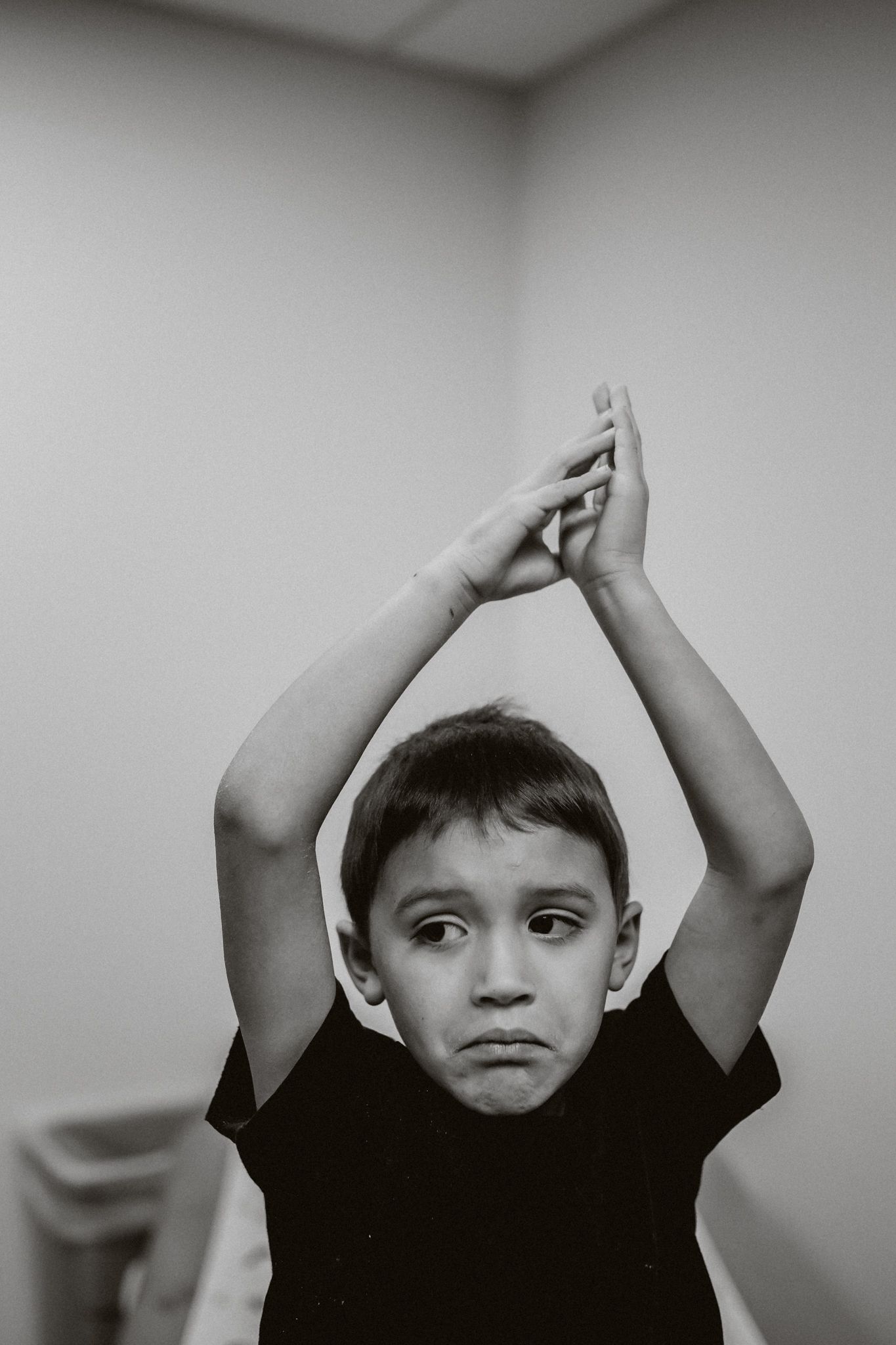A black and white photo series showing a child with raised arms making shapes against a plain wall background.