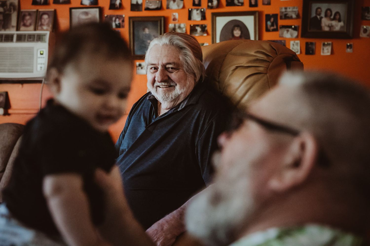 People gathered in a room with orange walls covered in family photographs.