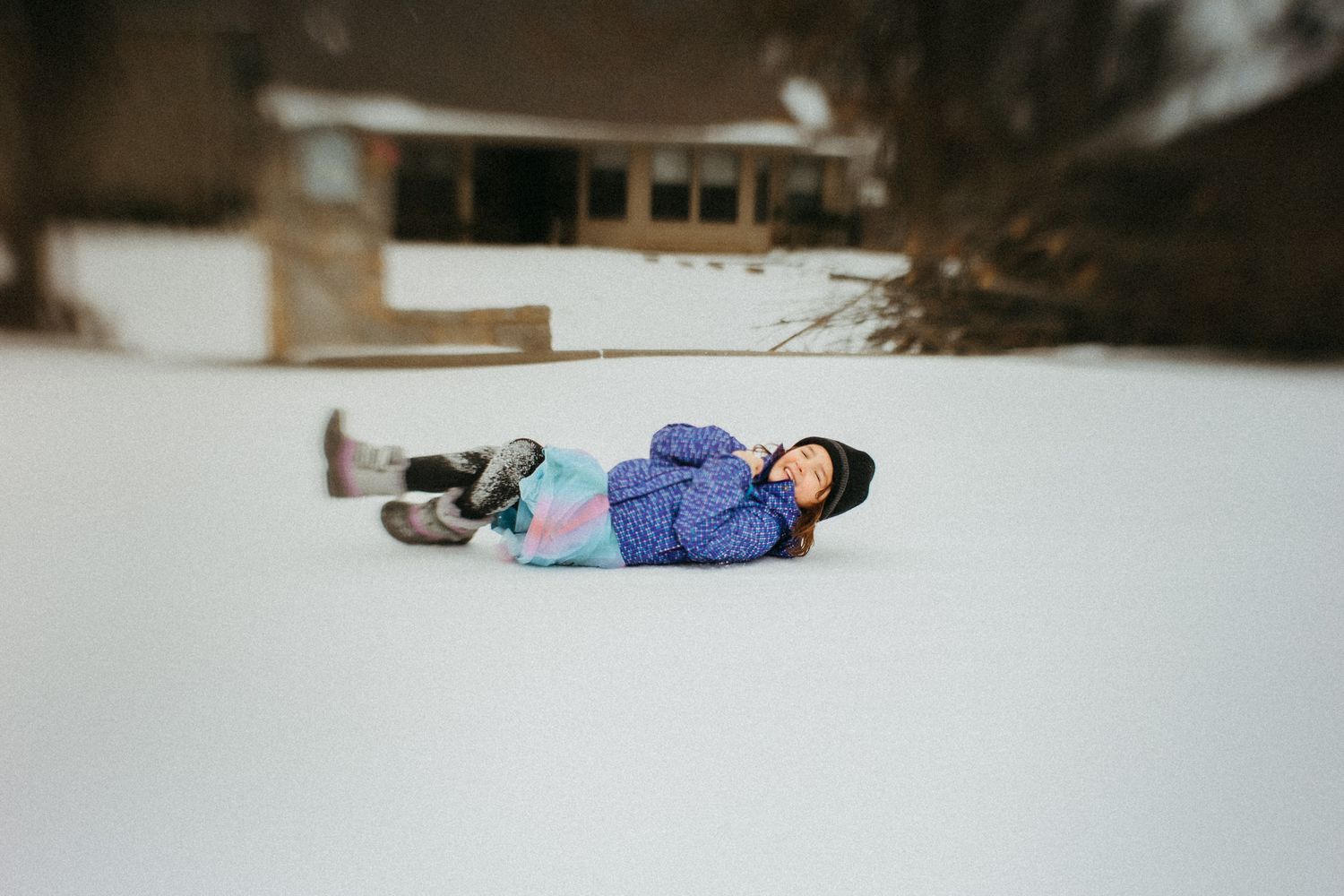 Person lying in snow wearing blue winter coat during outdoor winter activities.