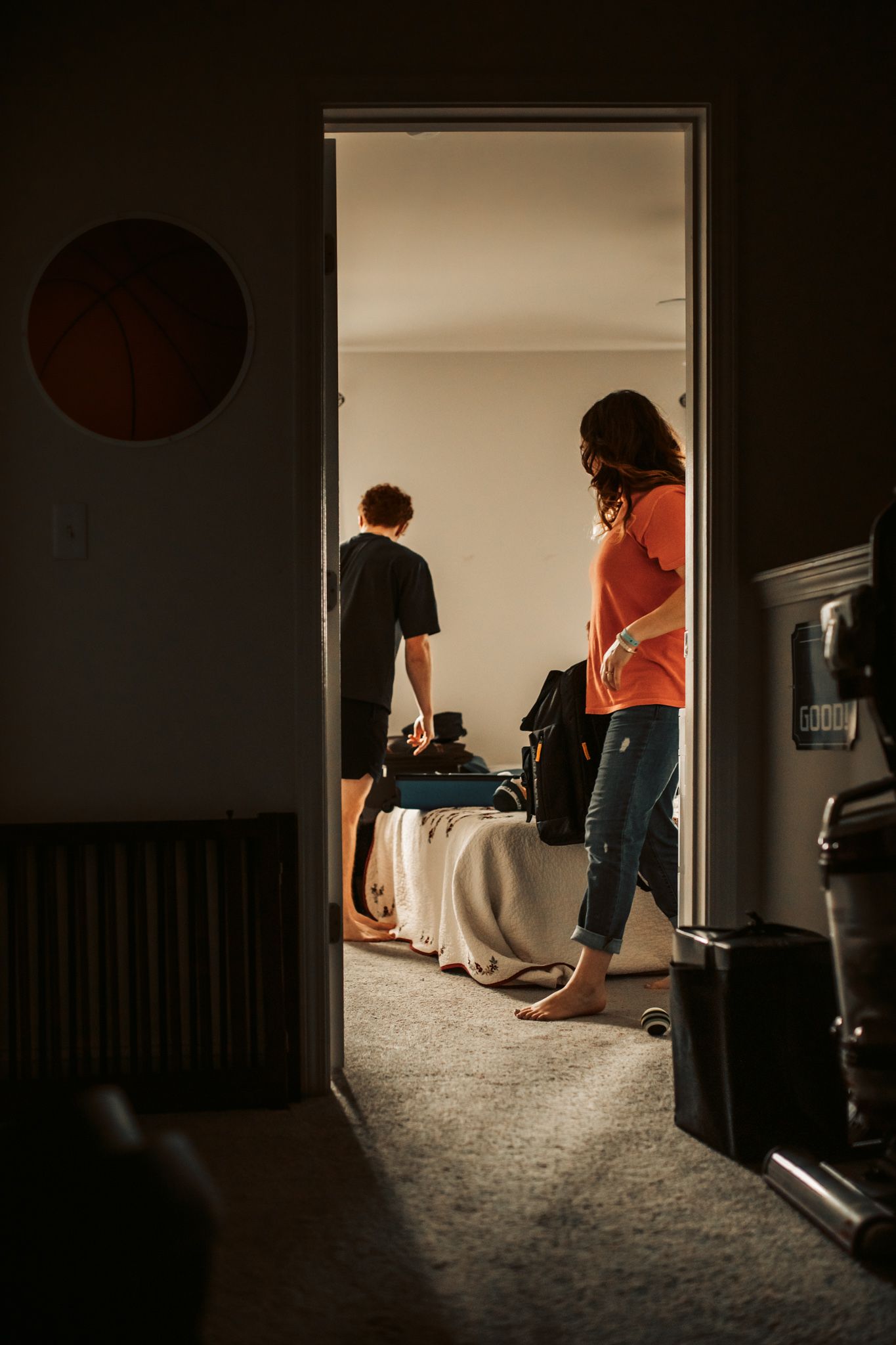 Side view through doorway of two people standing near furniture in warm lighting. In-Home Photography Liz Perez