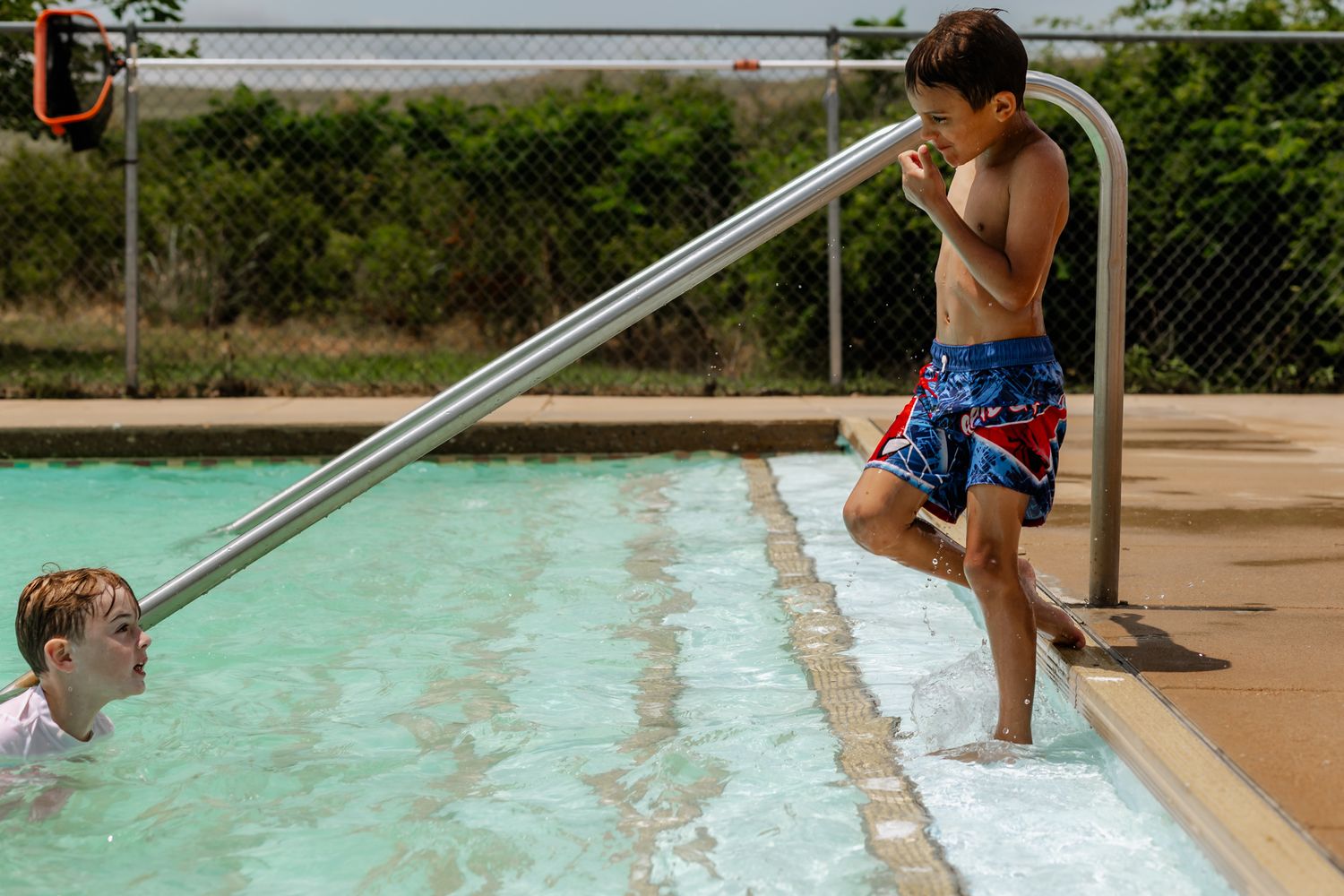 Young swimmers lined up at the edge of a pool preparing to jump in on a sunny day.
