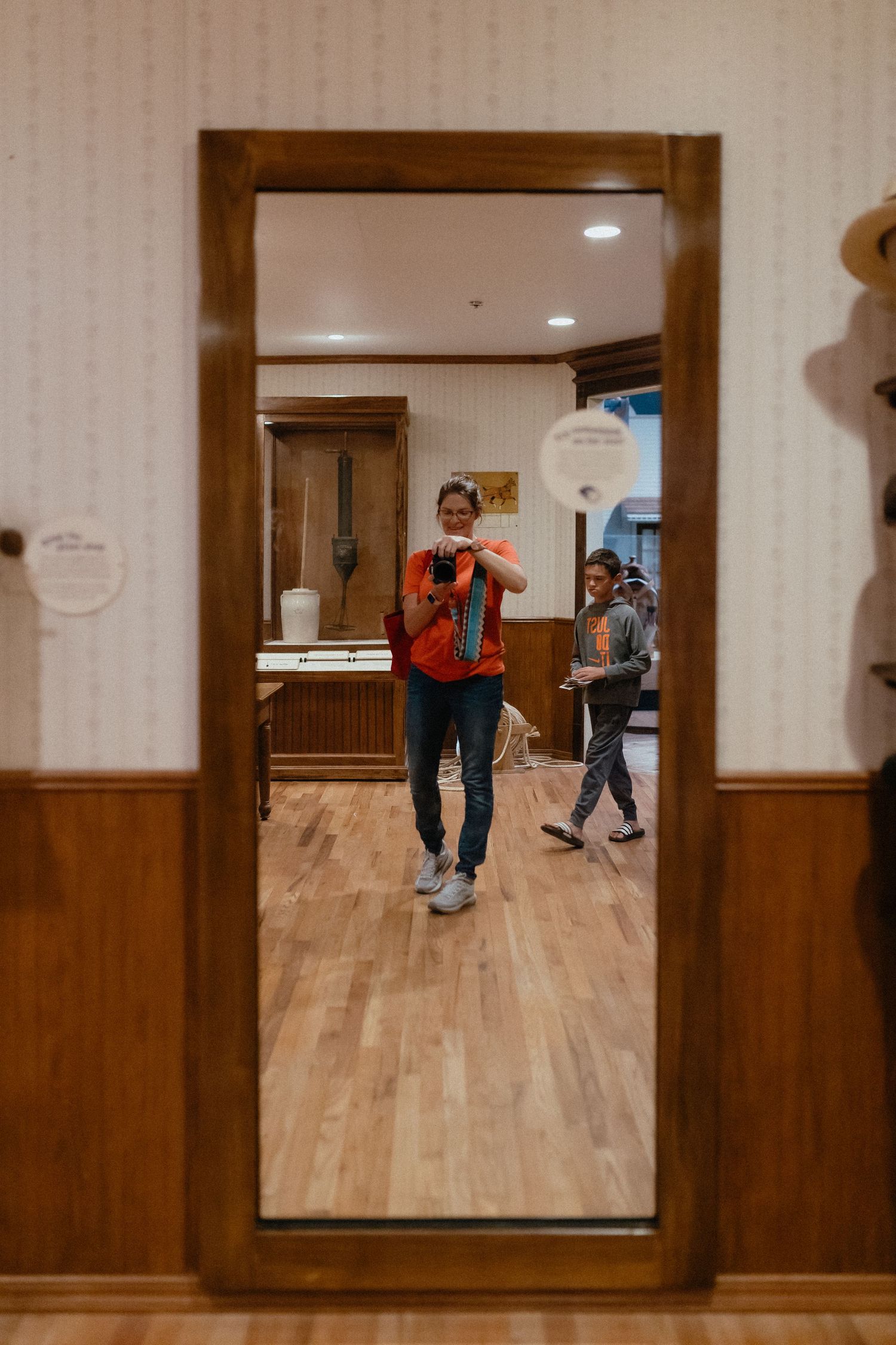 A mirror reflection shows dancers practicing in a wooden-floored studio with brown paneled walls.