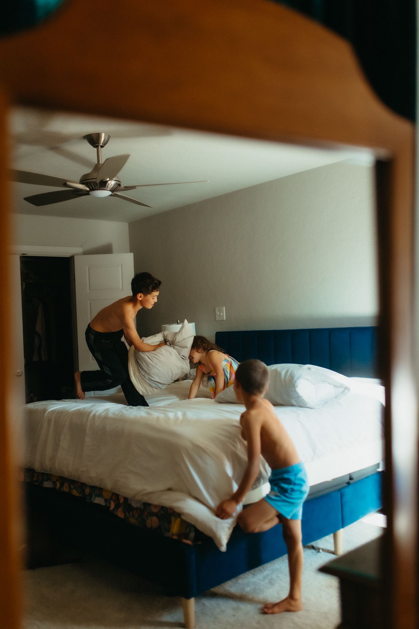 People having fun jumping on a large bed in a blue-walled room.