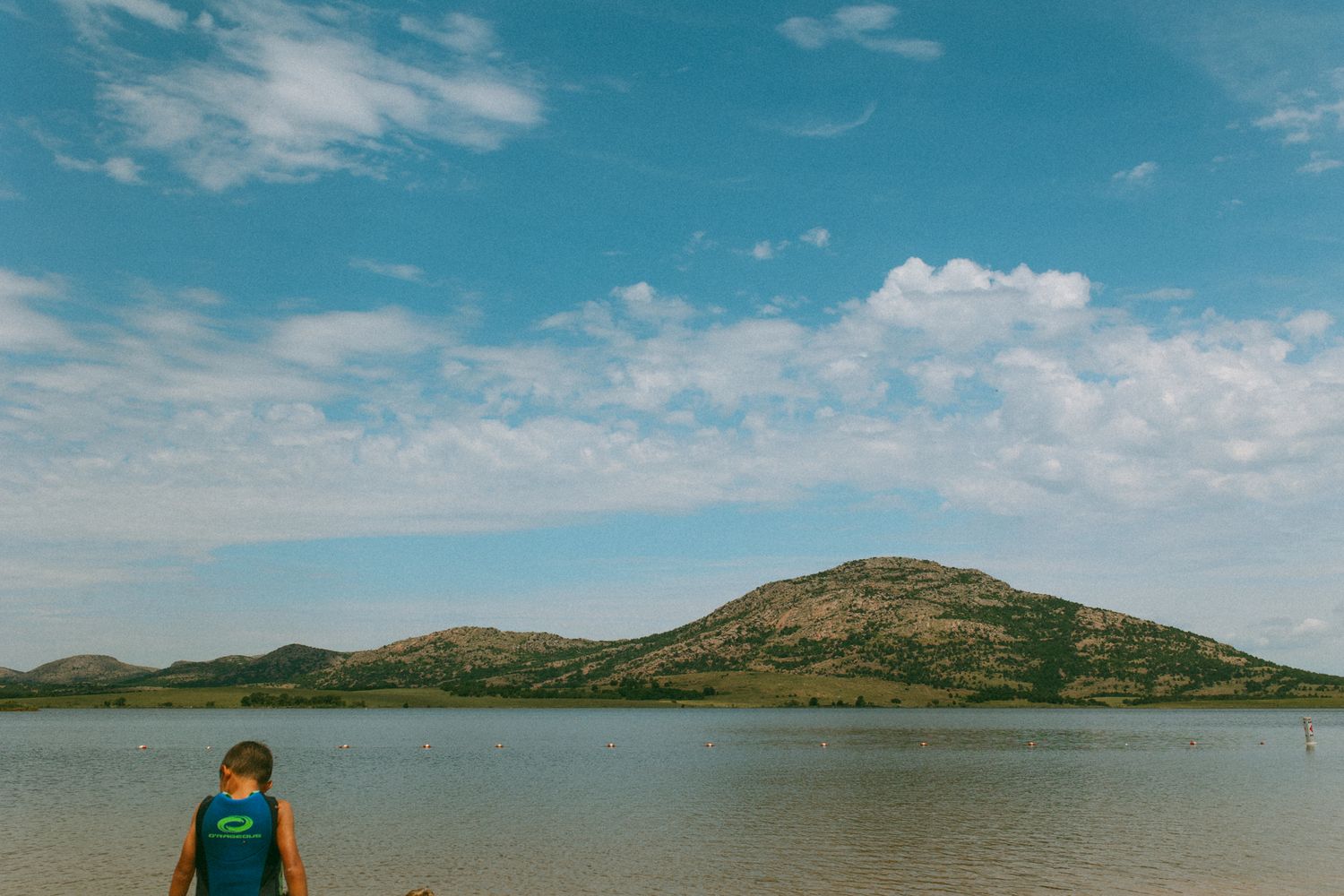 Lake landscape view with mountain backdrop and blue summer sky.