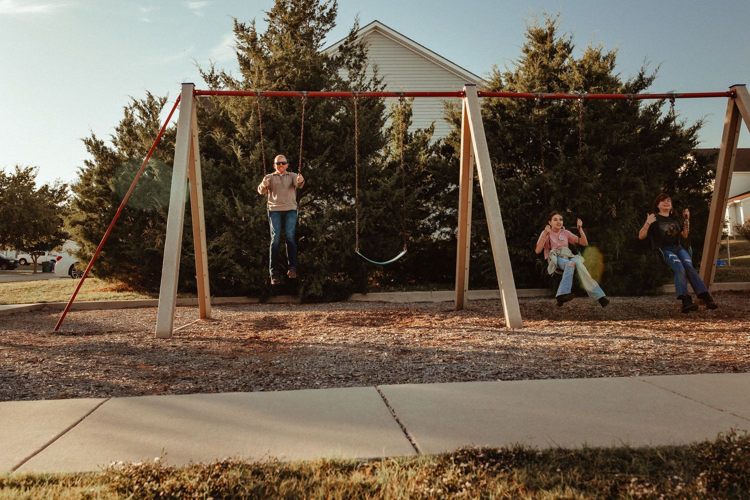 Children playing on swings at a neighborhood playground during sunset.