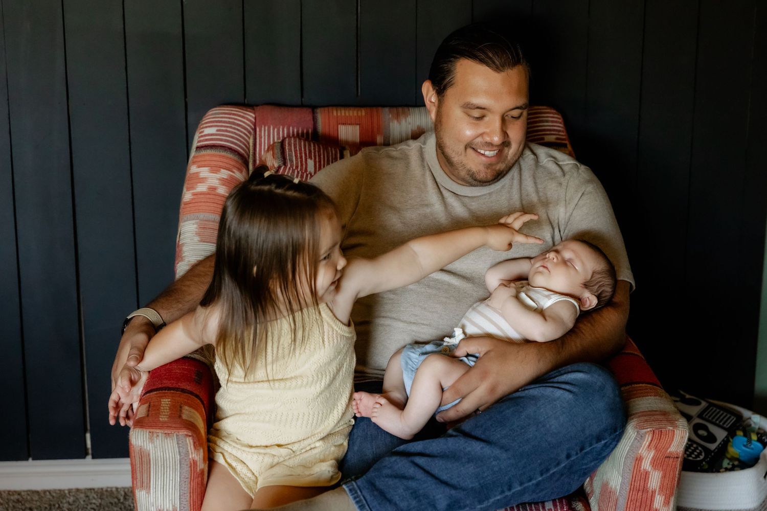 Family relaxing together on dark couch with newborn baby.