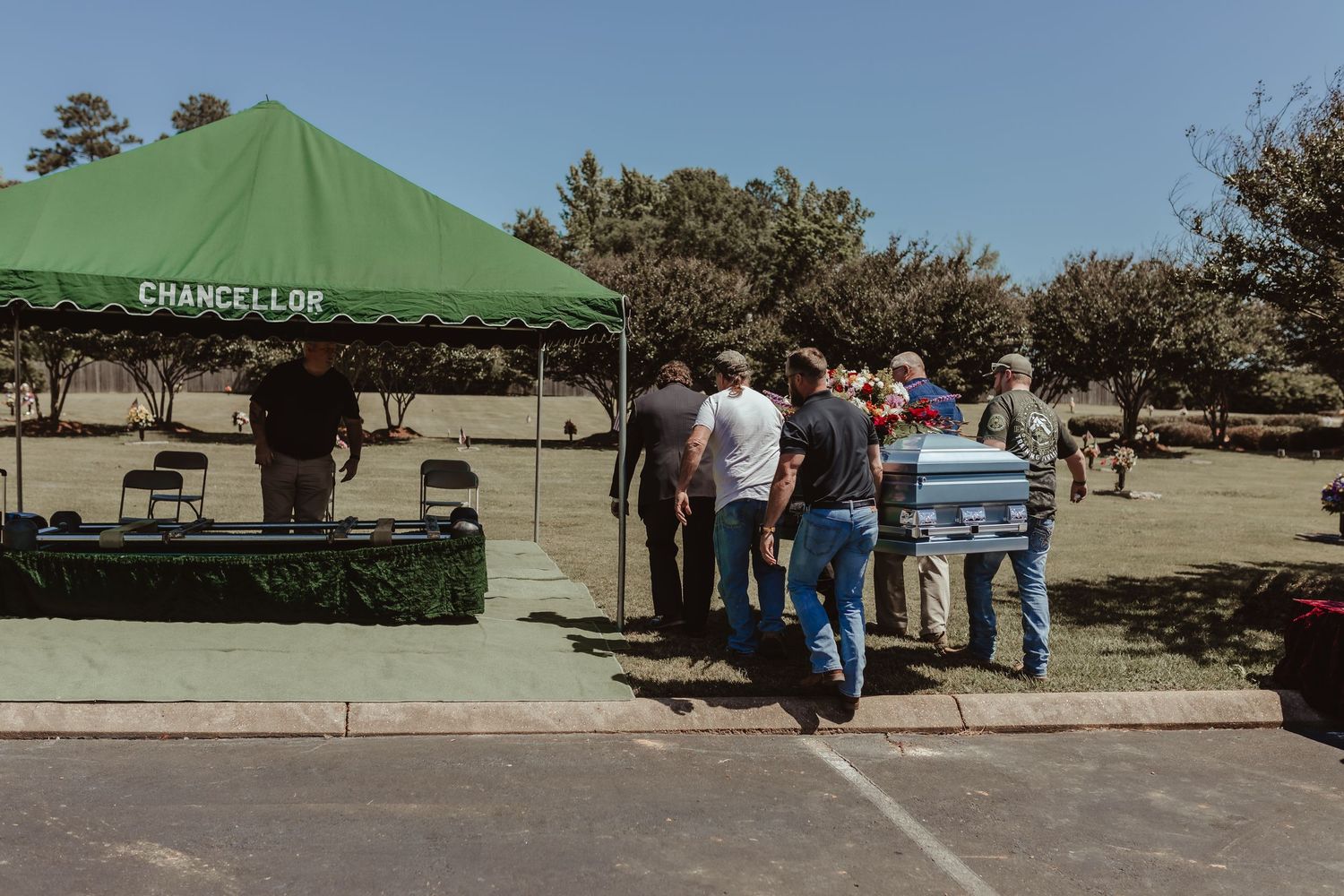 People waiting in line at an outdoor venue under a green tent canopy.