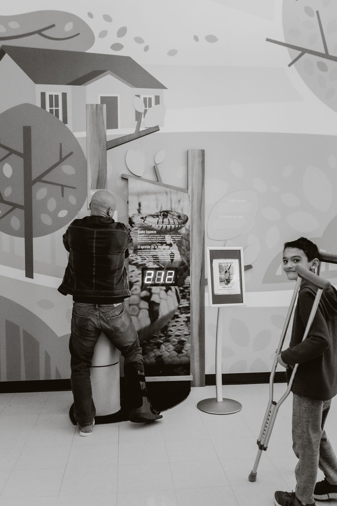 People looking at black and white artwork on a wall in a gallery-like setting with crutches visible.