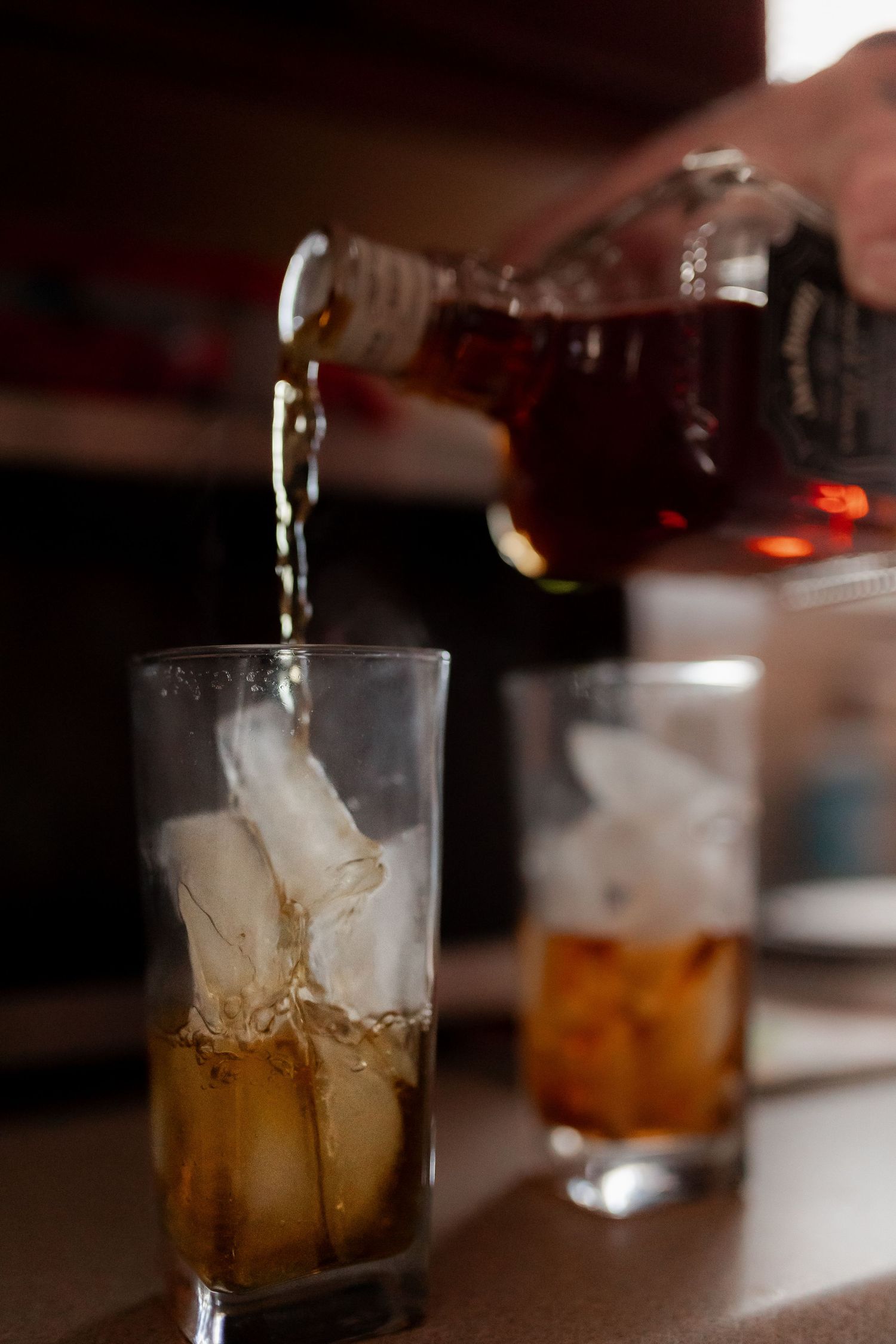 Dark liquid being poured from a bottle into a glass with ice cubes.