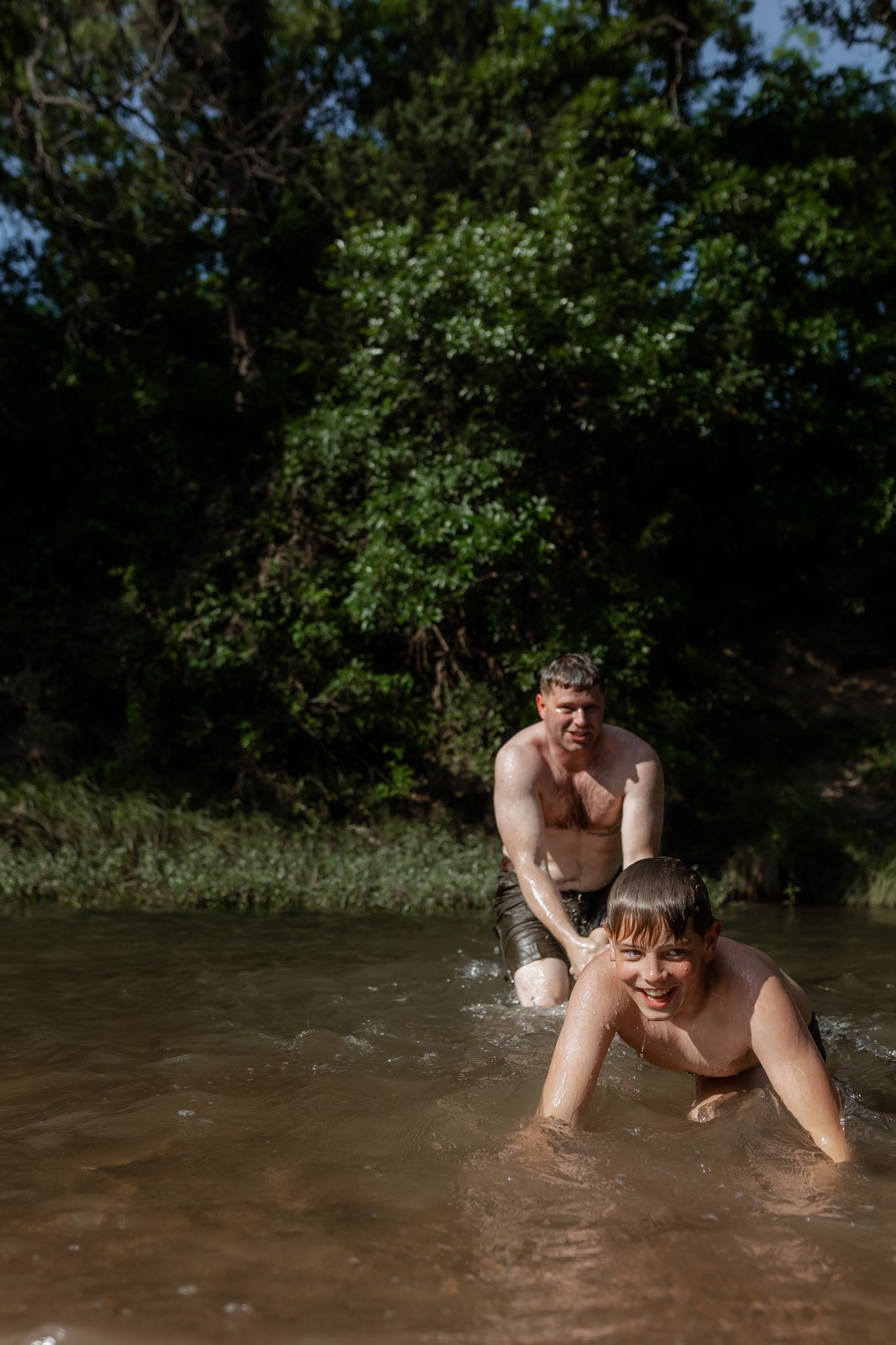 Two people splashing and playing in shallow river water on sunny day.