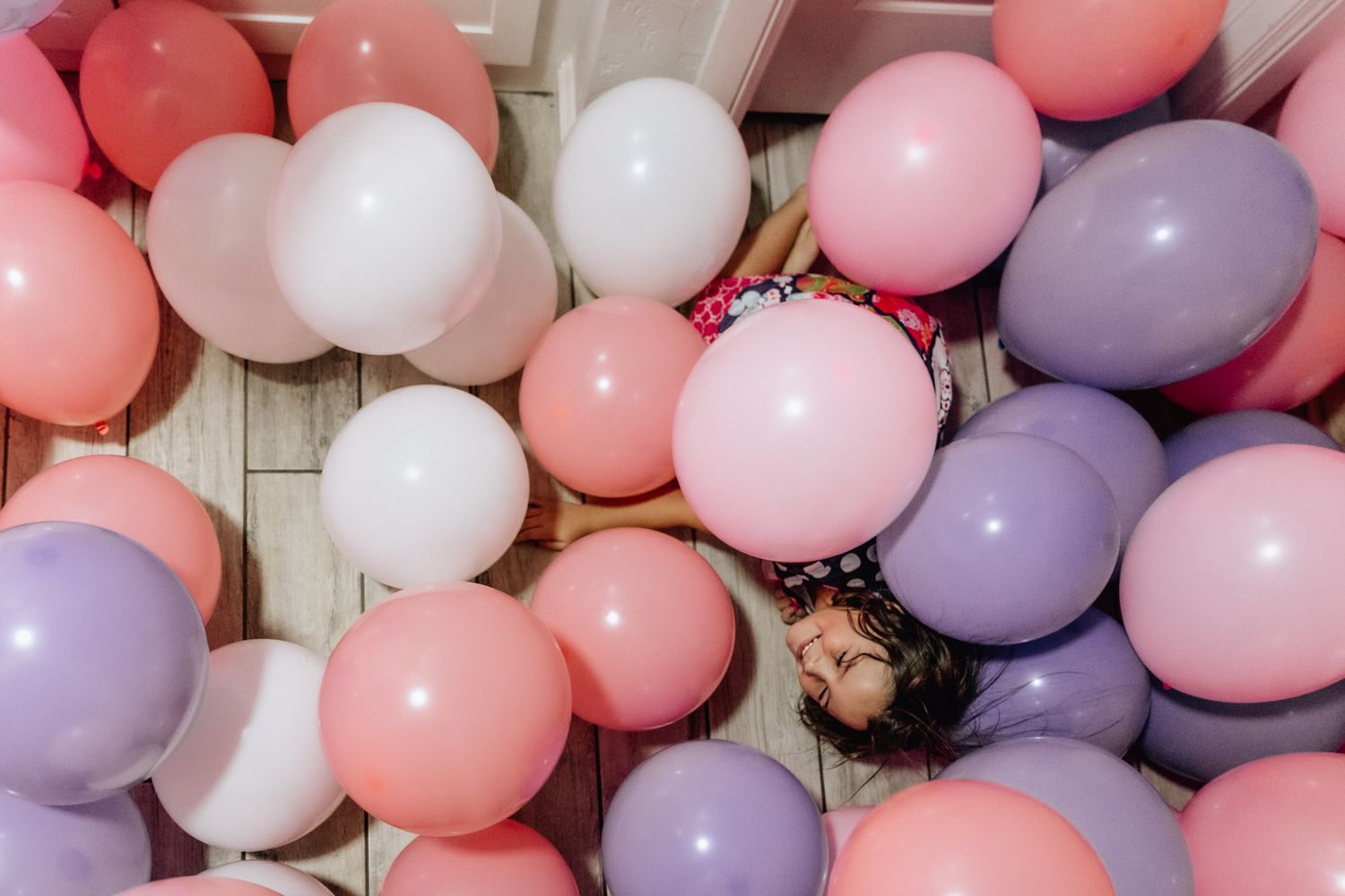 A festive balloon arch installation featuring pink, purple and white balloons against a light background.