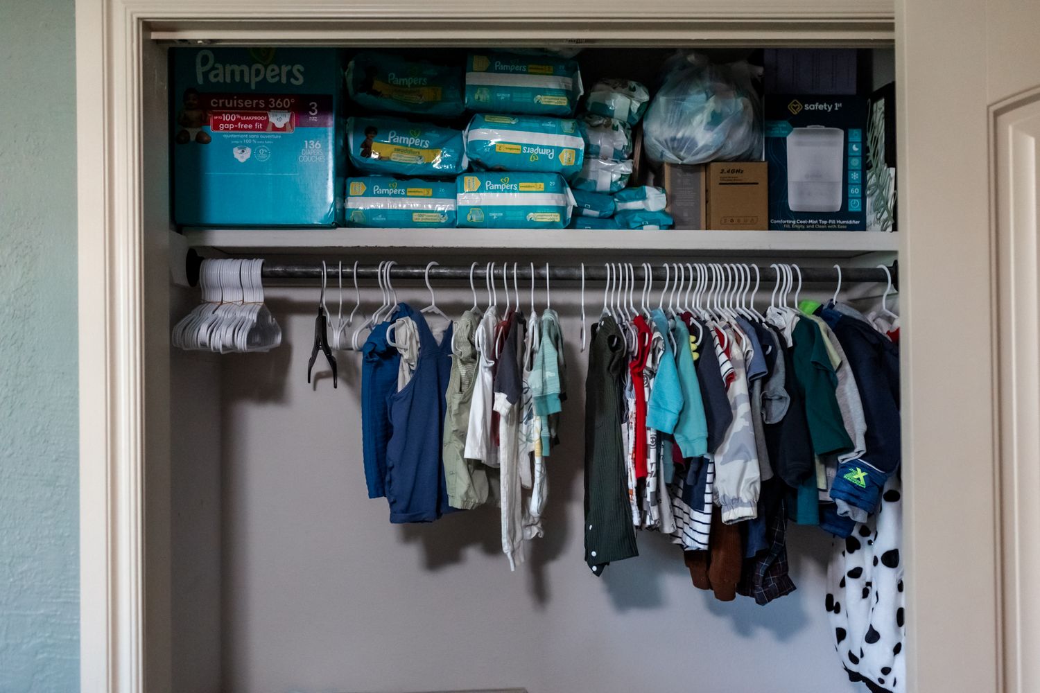 An organized closet with hanging children's clothes and blue storage bins on the upper shelf.