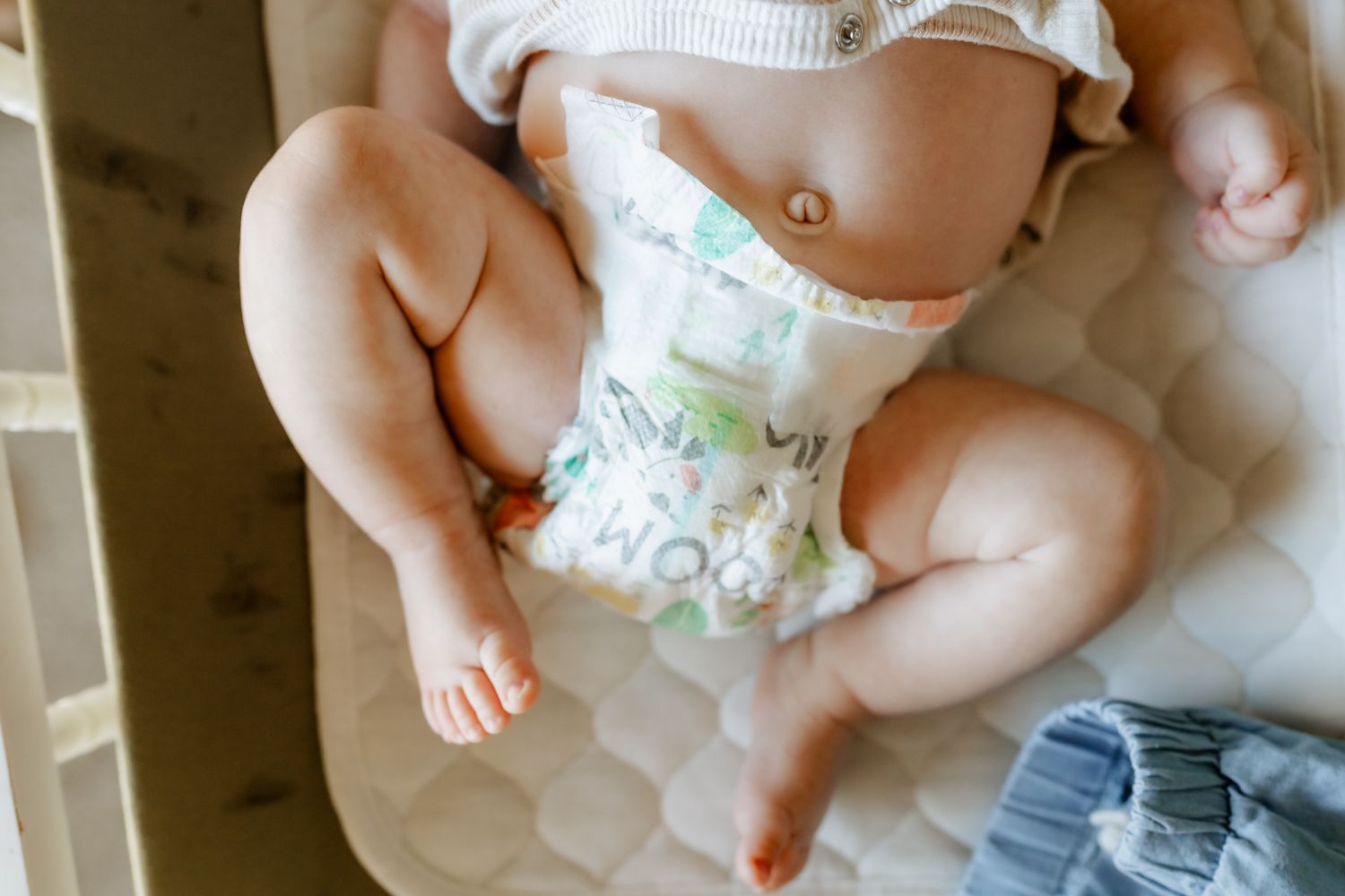 Baby wearing a disposable diaper sits on a mattress or cushioned surface.