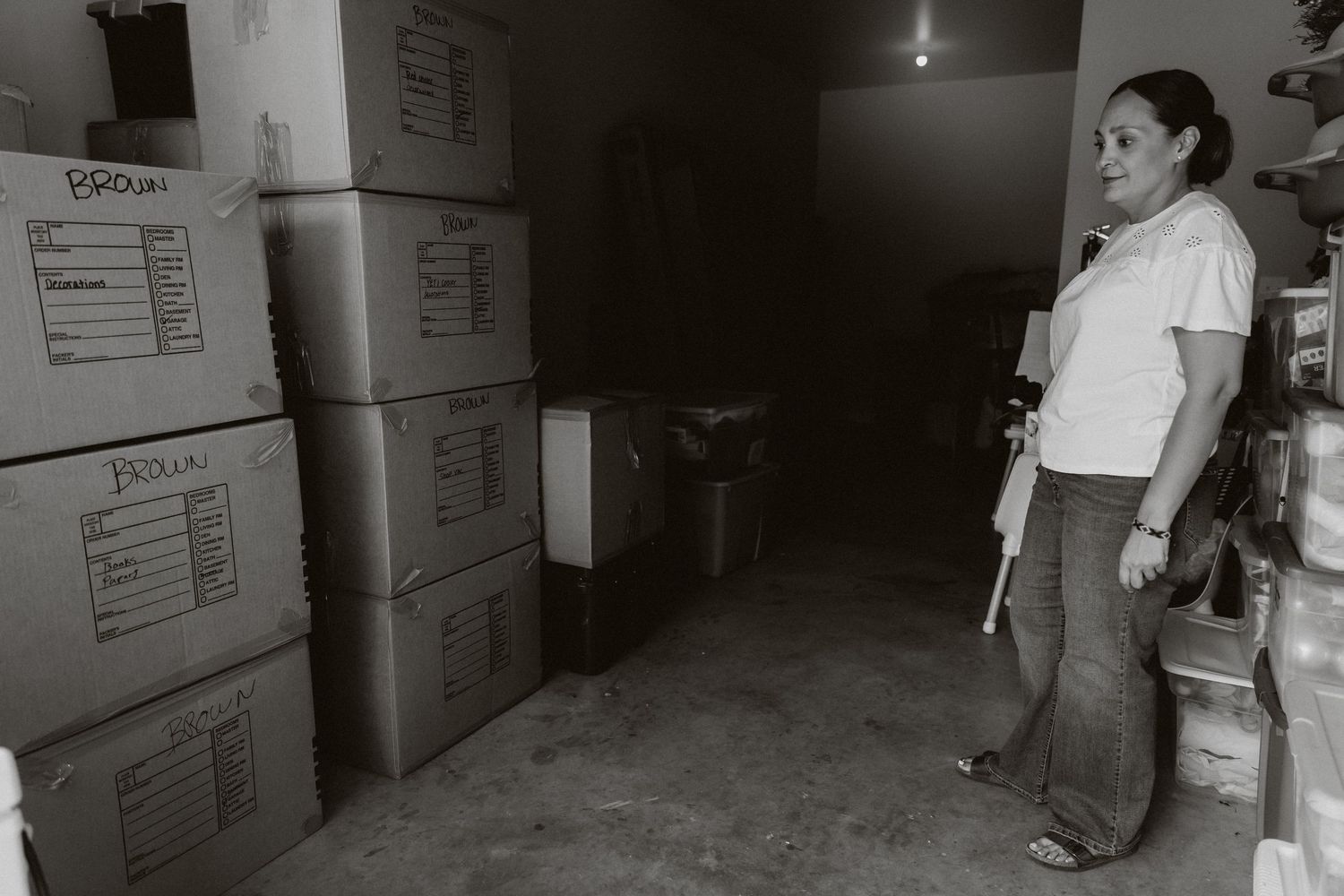 Woman standing in a storage room surrounded by stacked cardboard boxes in a black and white photo.