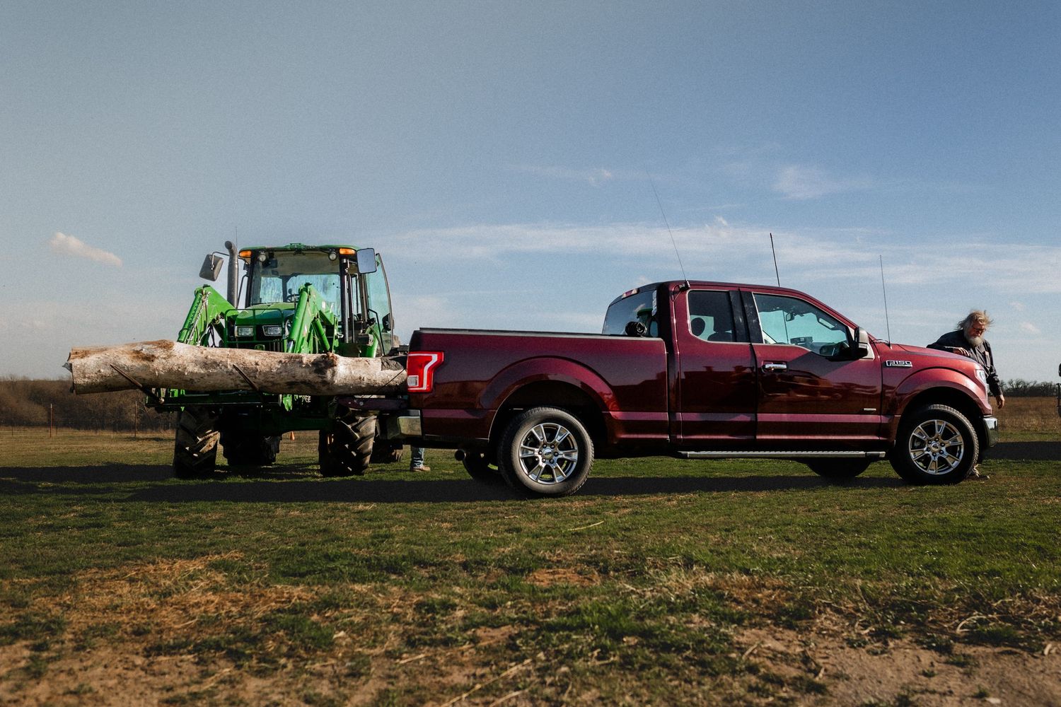 Agricultural equipment and pickup trucks parked in a field under blue sky.