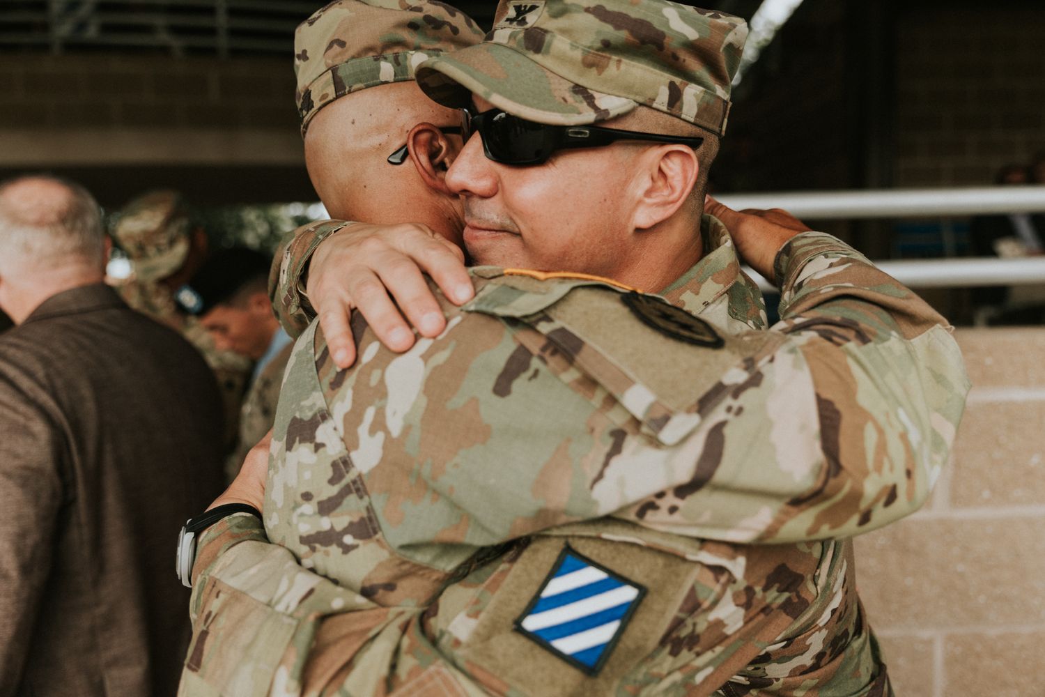 Two soldiers in camouflage uniforms share an emotional embrace, with one wearing the 3rd Infantry Division patch.