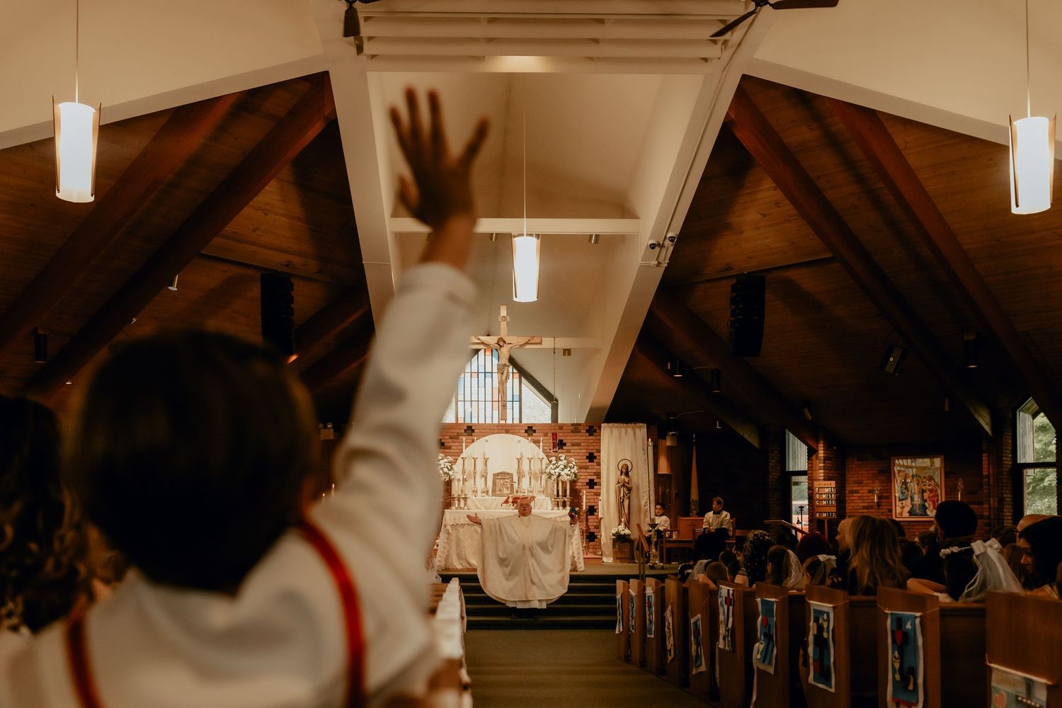 A raised hand silhouetted against warm lighting in a church sanctuary with wooden beams and pews.