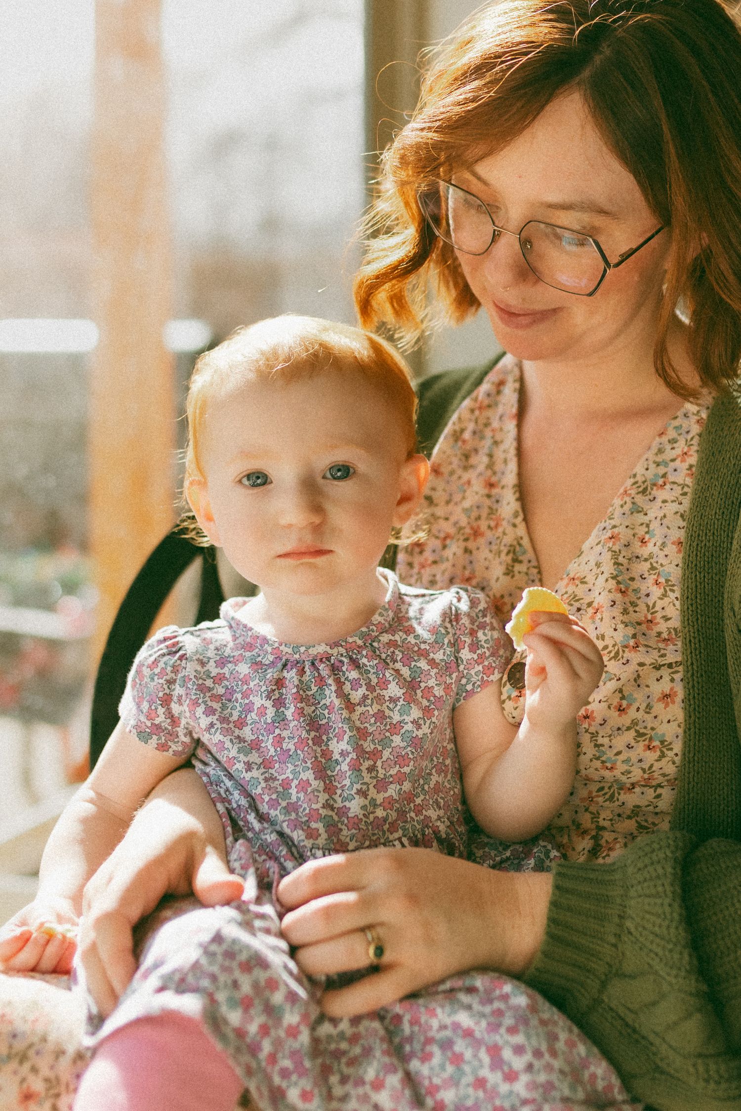 A series of warm-toned photos showing a baby in a floral dress being held while sitting near a window.