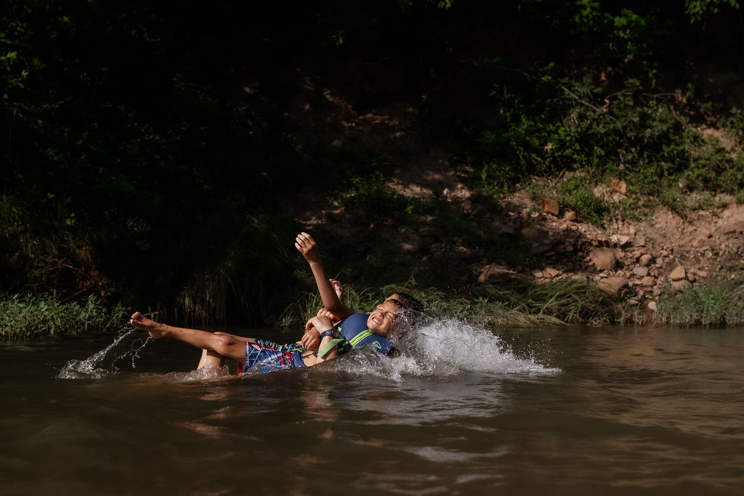 Person splashing and playing in a natural swimming hole on a summer day.