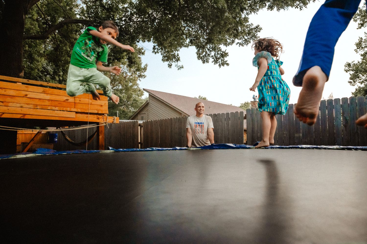 Children jumping and playing on a large backyard trampoline on a sunny day.