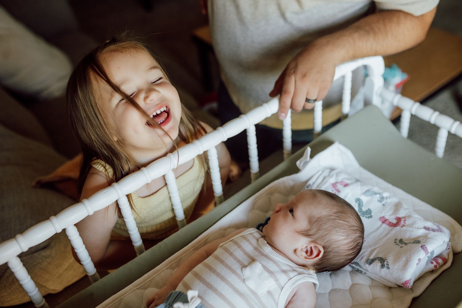 Sweet moment of joy shared between siblings near a white crib.