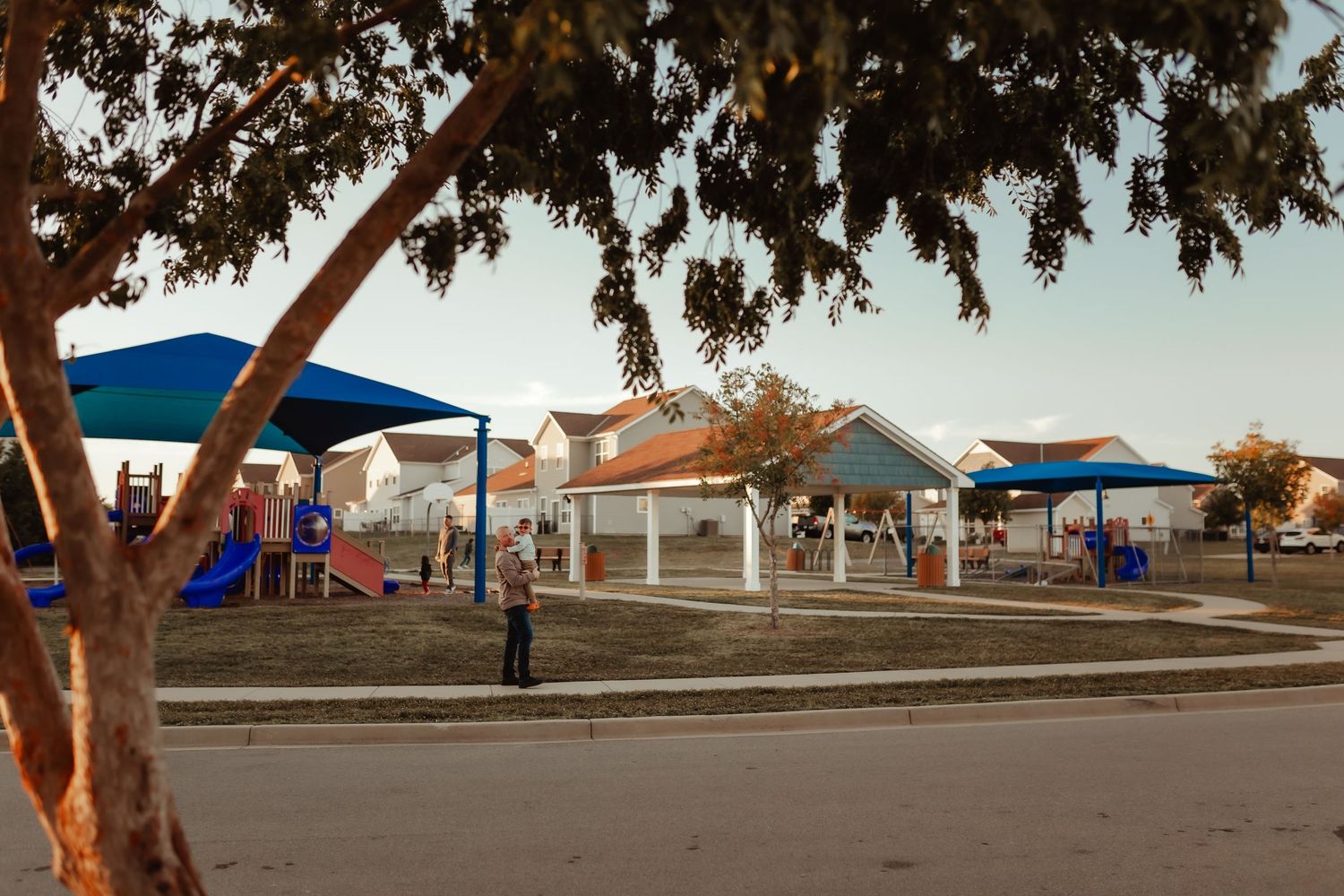 A community playground and gathering area with blue canopies and trees at sunset.