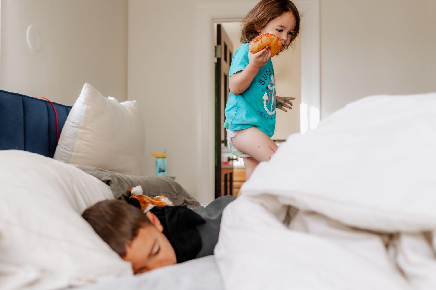 A carefree moment at home as someone in a turquoise shirt playfully peeks into a bedroom where child sleeps.