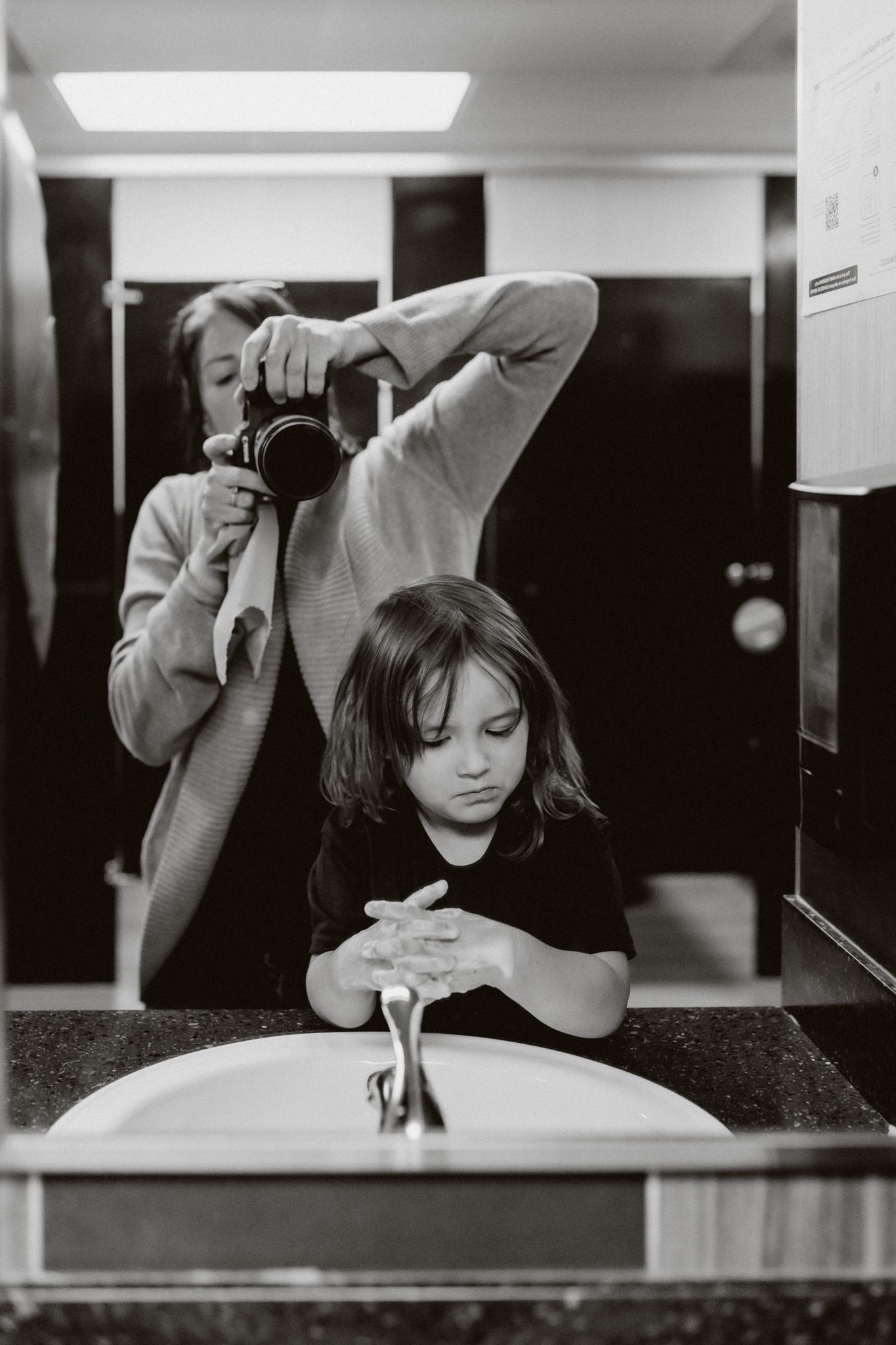 Black and white photo of a child washing hands at a sink while mom and photographer documents this milestone of growing up, Liz Perez Photog